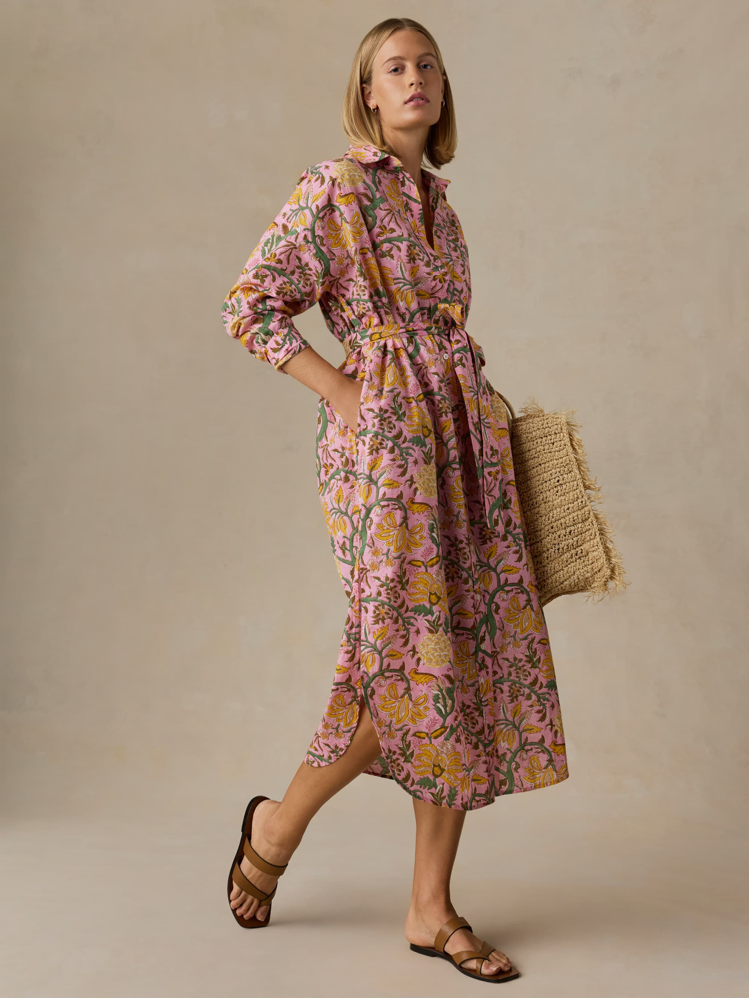 Woman wearing a floral dress holding a woven bag against a beige background
