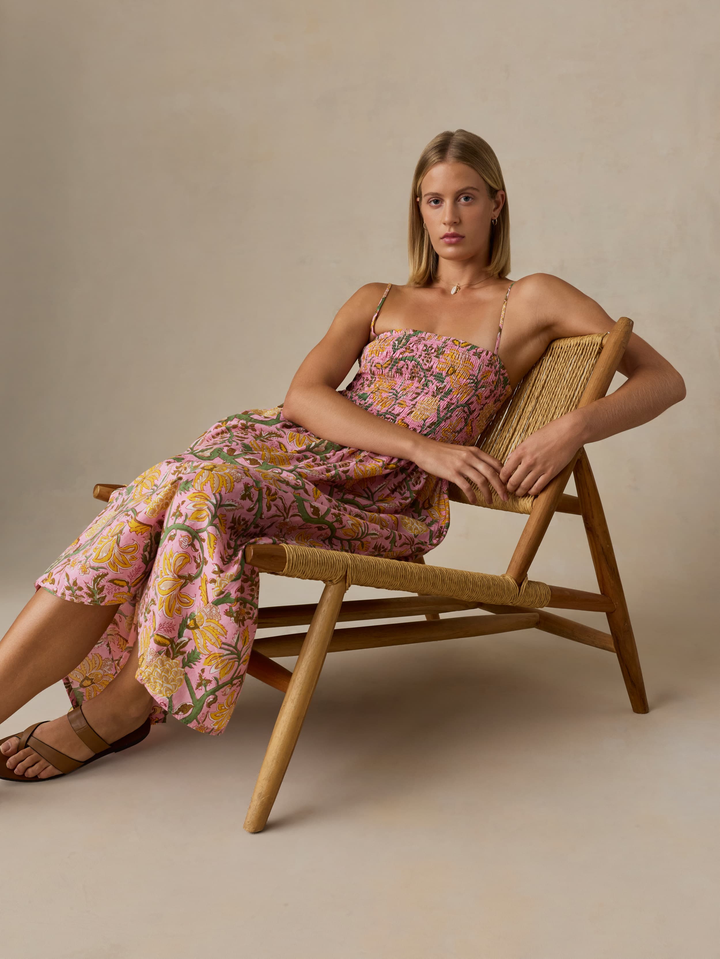 Woman in a floral dress sitting on a wooden chair against a beige background