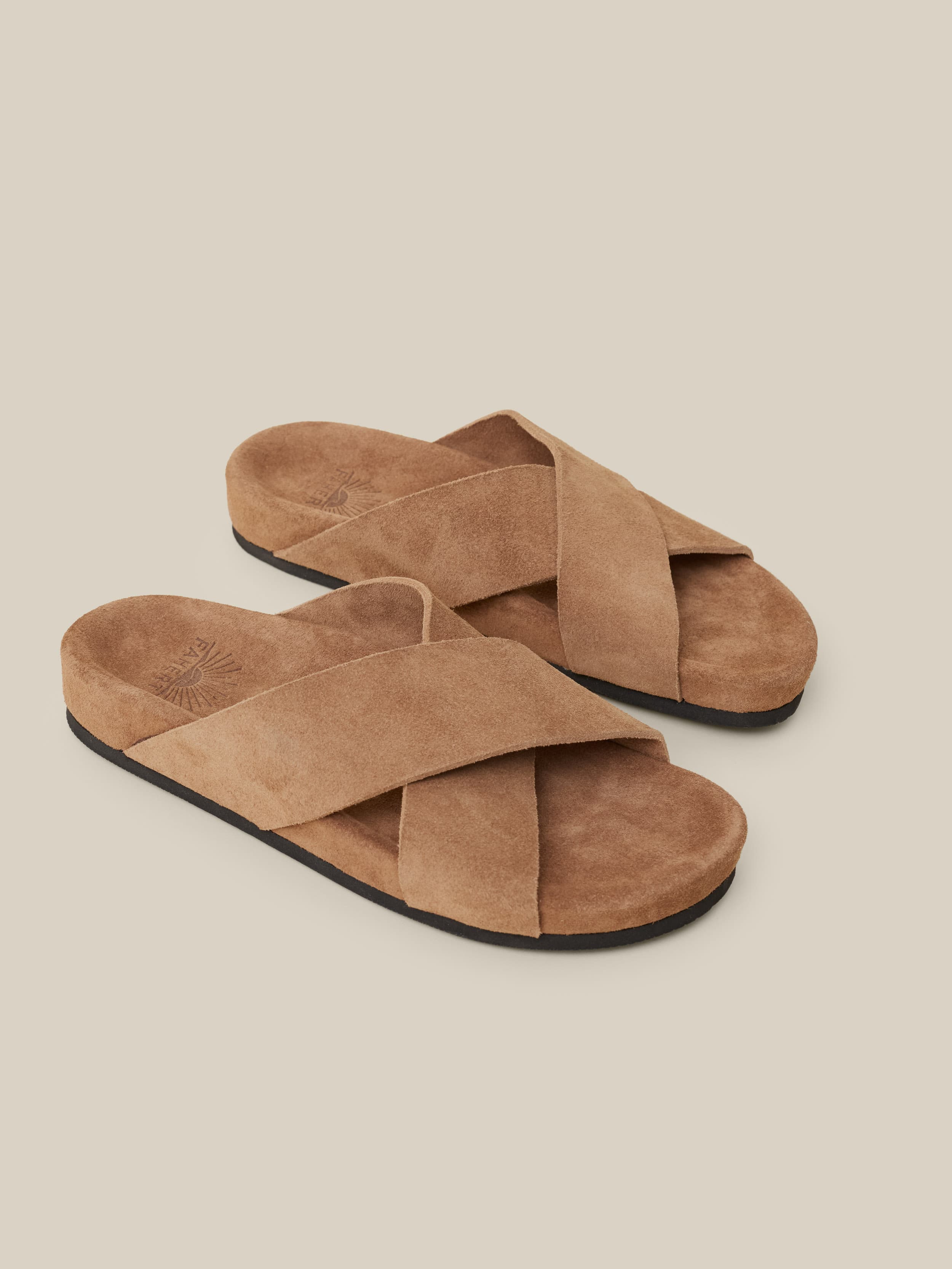 Brown suede sandals against a beige background
