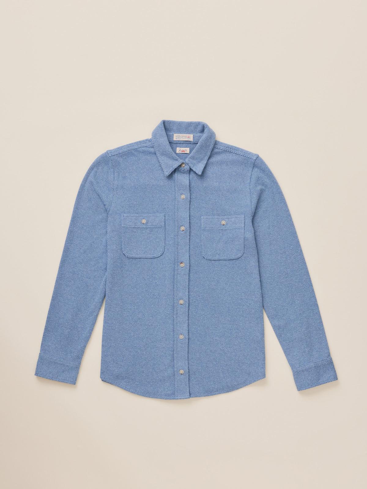 A light blue long-sleeve button-up shirt with two chest pockets, laid flat against a solid beige background., image 6 of 7
