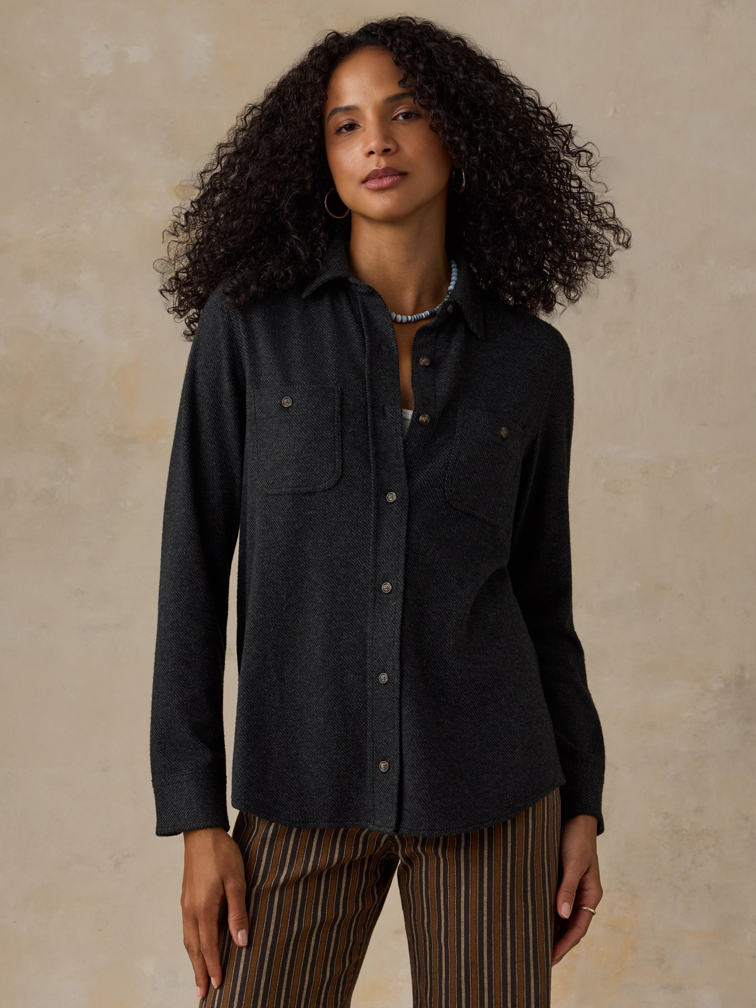 Woman wearing a black sweater shirt with brown striped pants against a beige background