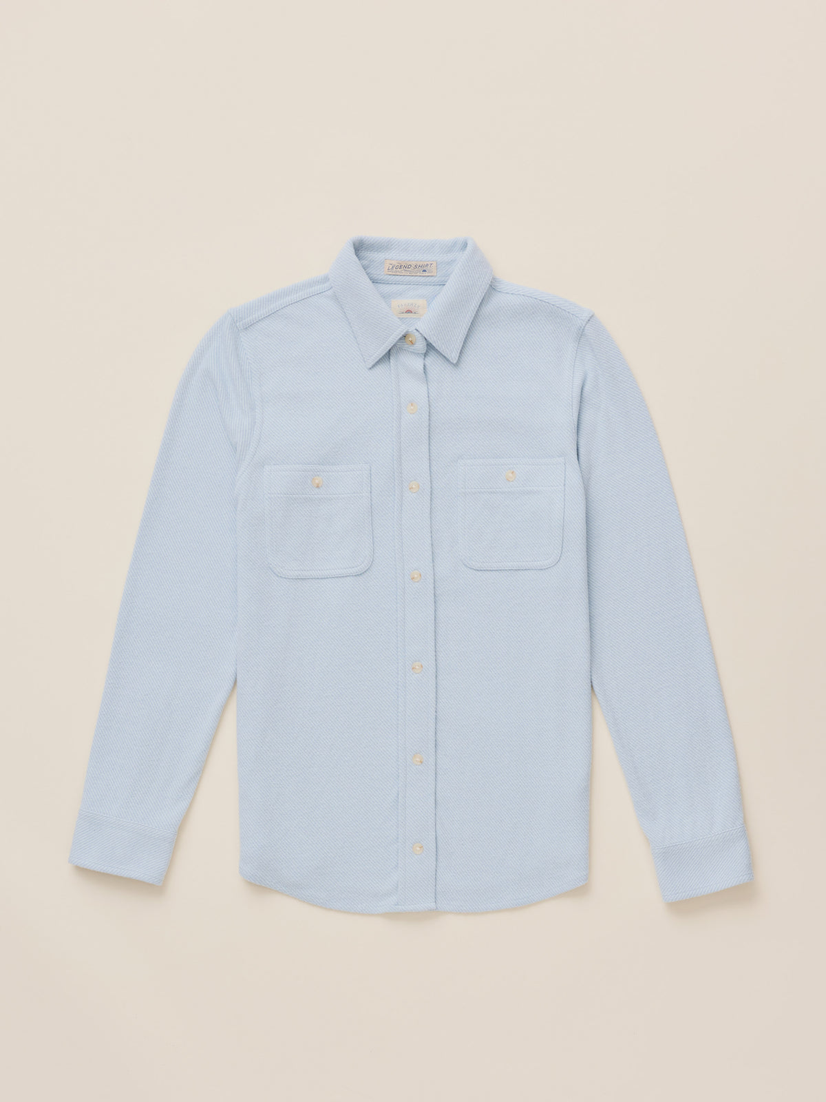 A light blue long-sleeve button-up shirt with two chest pockets, laid flat on a warm beige background., image 6 of 7