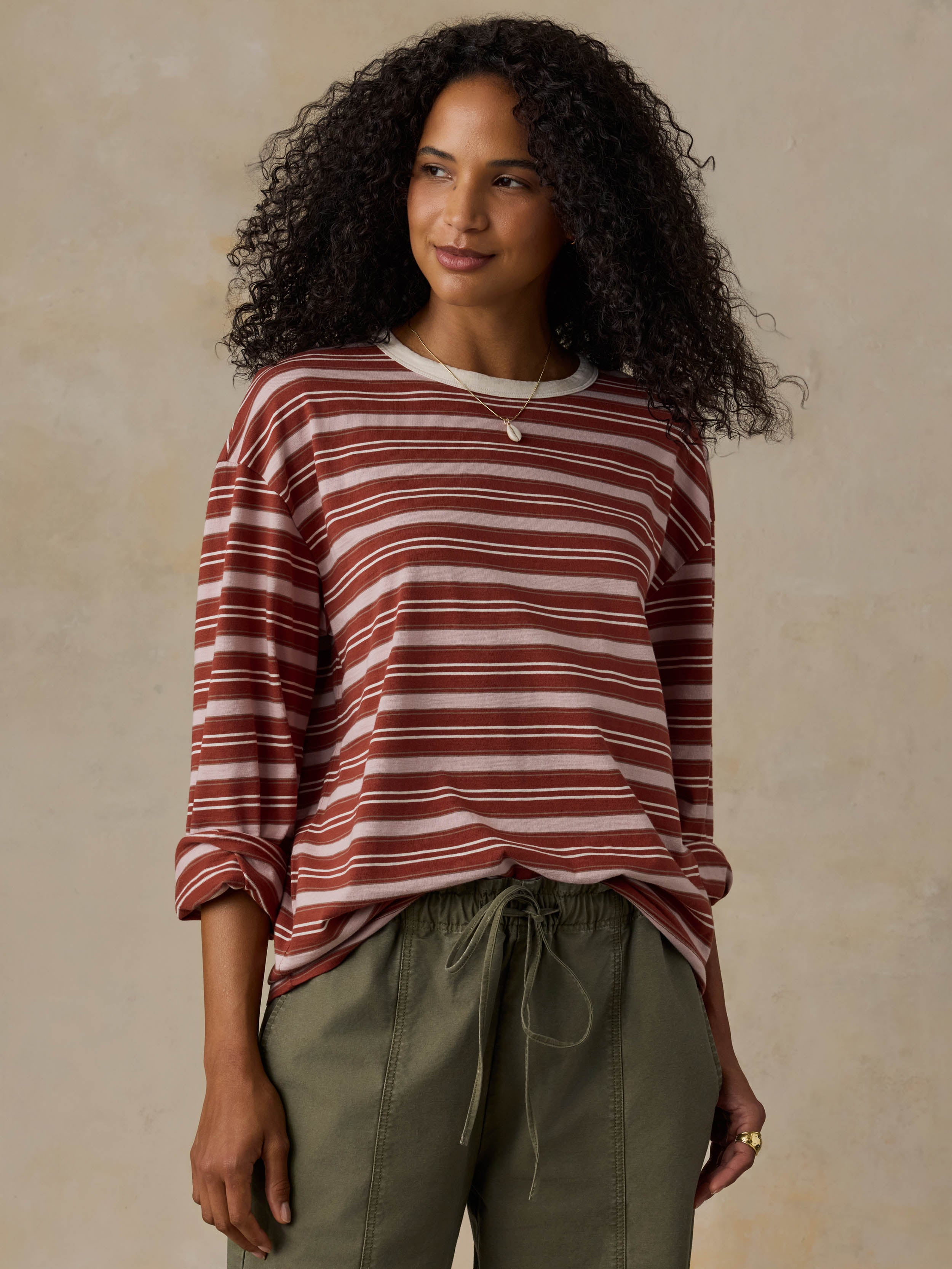 Woman wearing a red and pink striped long-sleeve shirt and green pants against a beige background