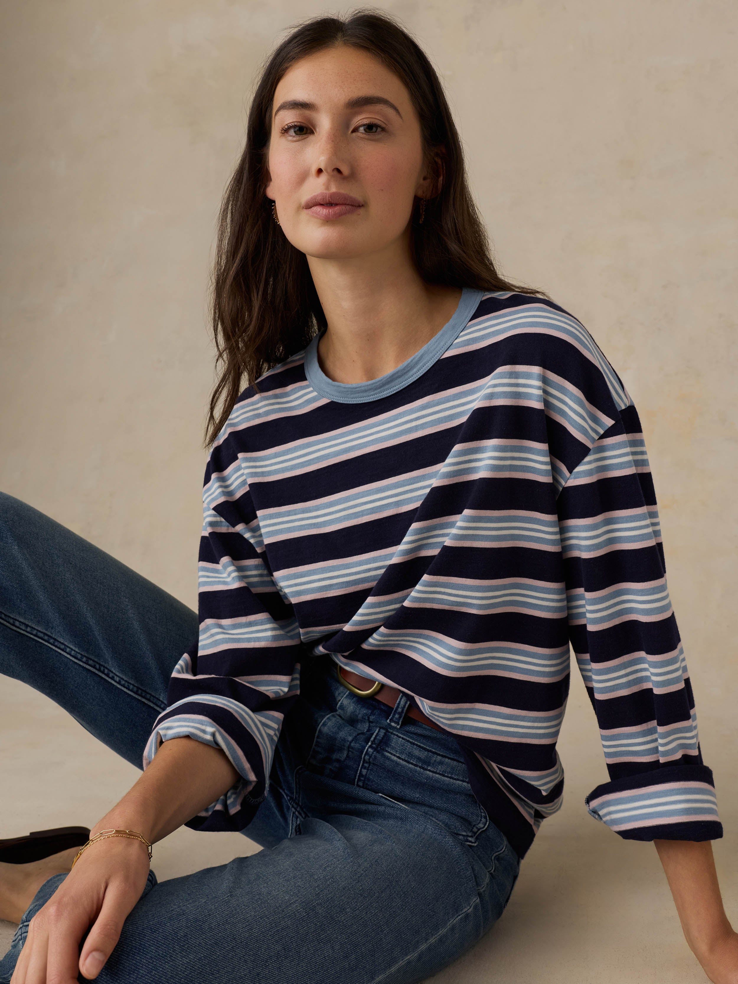 Woman wearing a blue striped shirt and jeans against a beige background