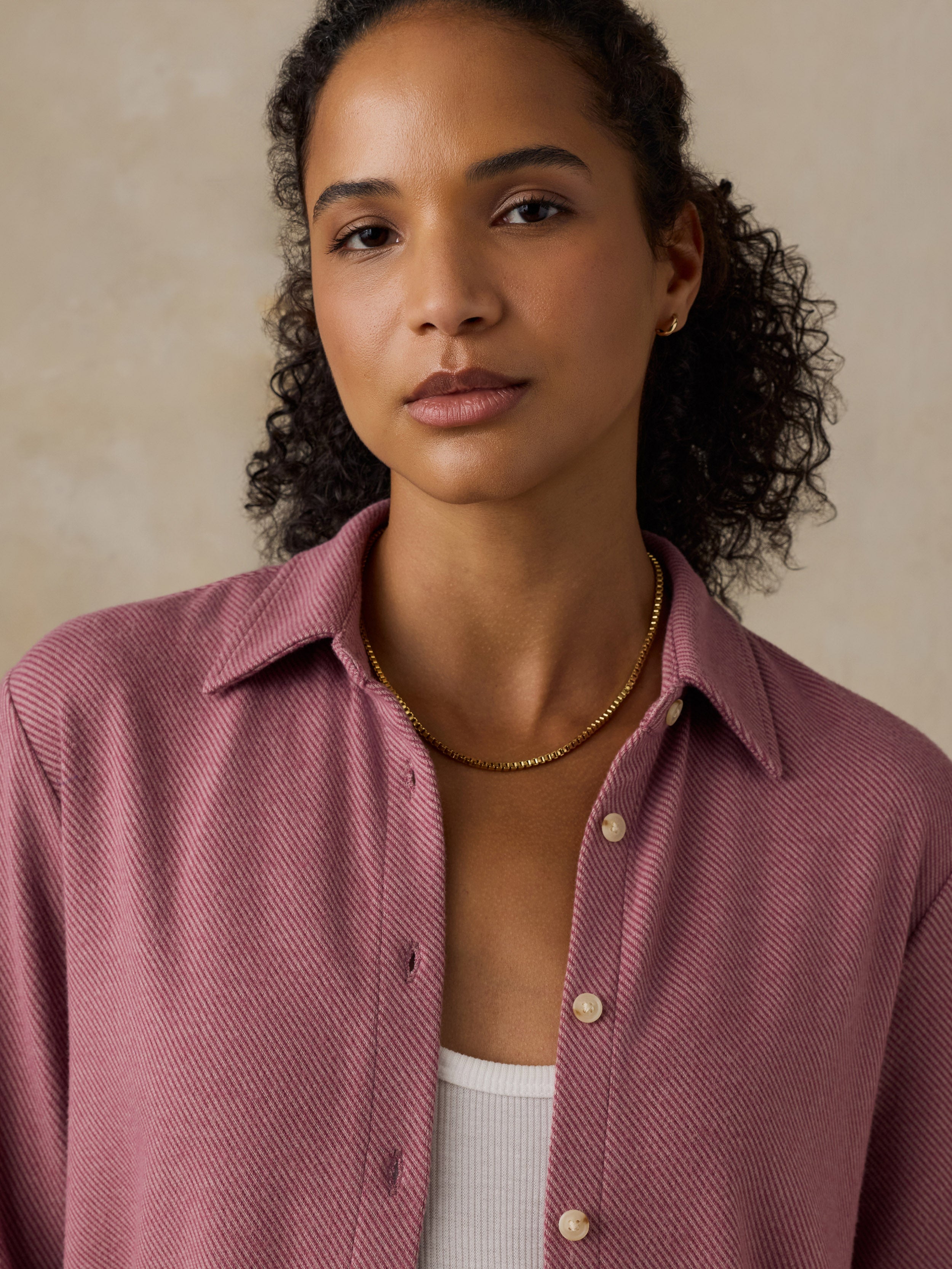 Woman wearing a pink button down shirt against a beige background