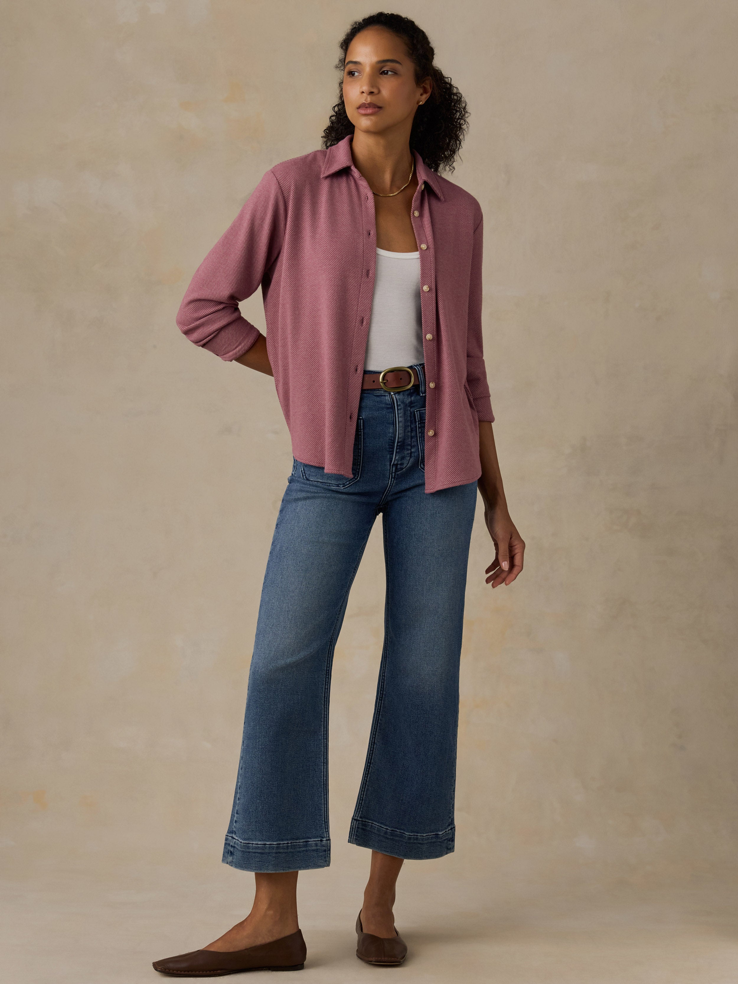 Woman wearing a pink button down shirt and blue jeans against a beige background