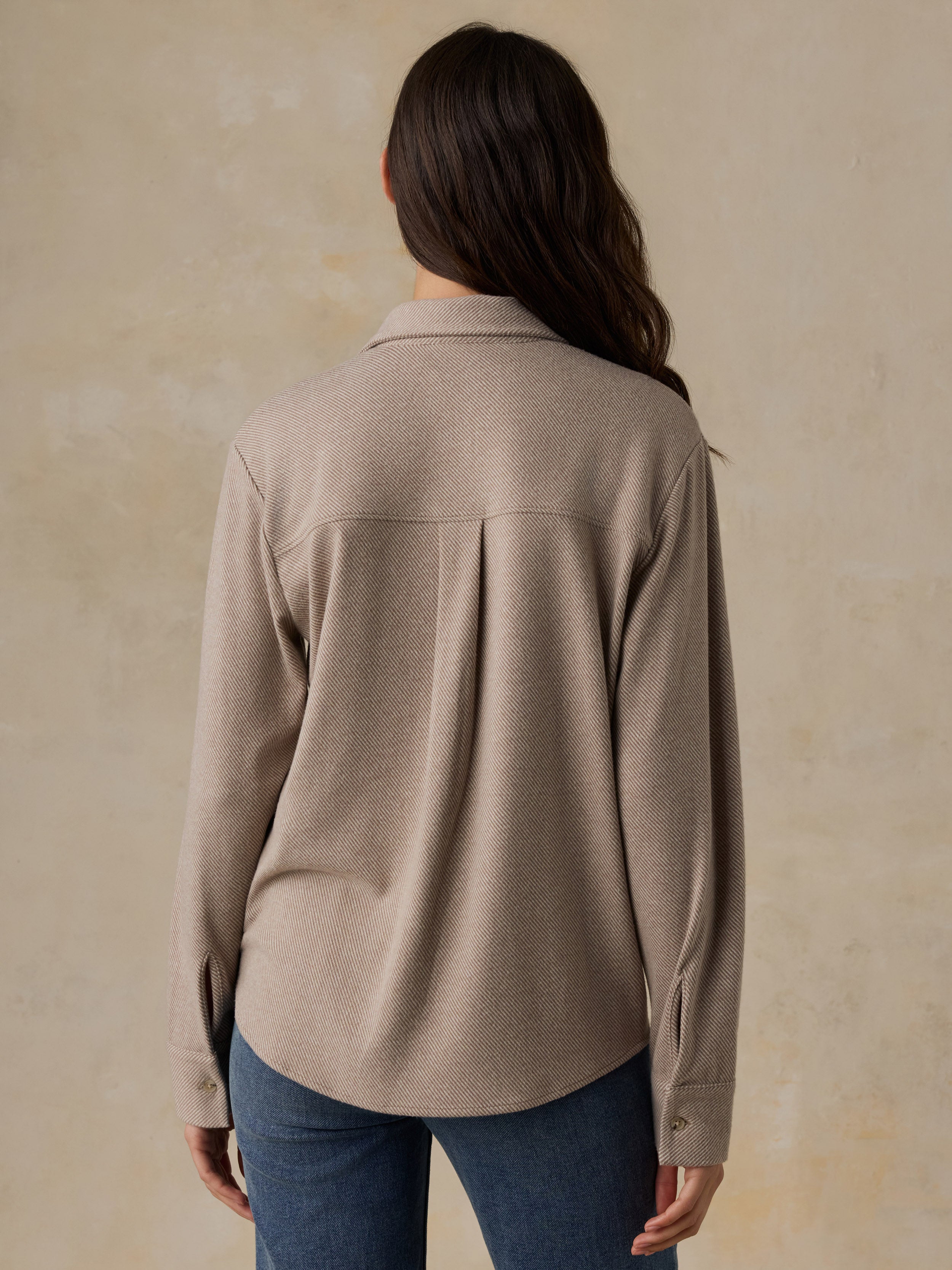 Woman wearing a beige button down shirt and blue jeans against a beige background