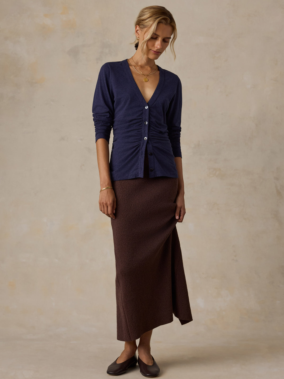 A woman wearing a blue long sleeve top, a brown skirt, and black flats, image 2 of 6