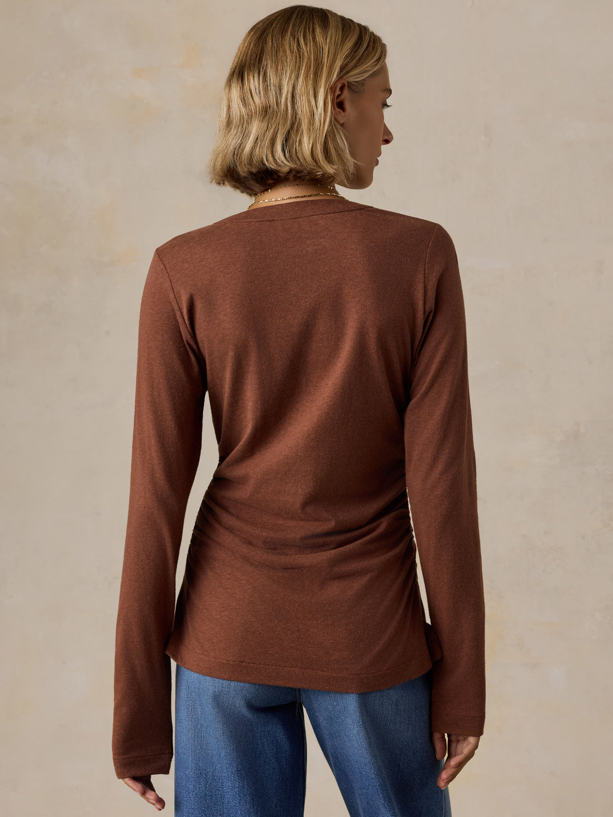 A woman viewed from the back wearing a brown long sleeve top and blue jeans, image 3 of 6