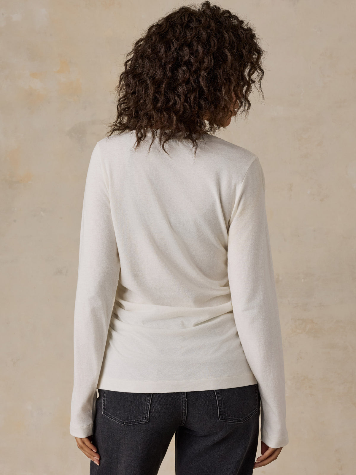 A woman viewed from behind wearing a white cardigan and black jeans, image 4 of 6