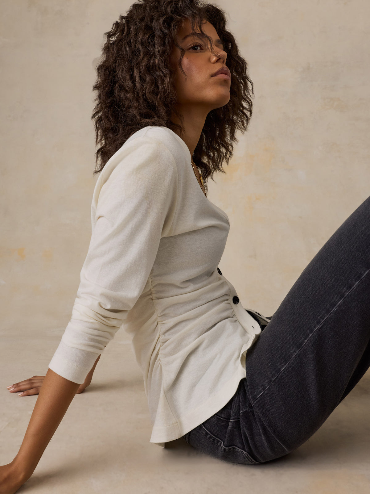 A woman sitting down wearing a white cardigan and black jeans, image 5 of 6
