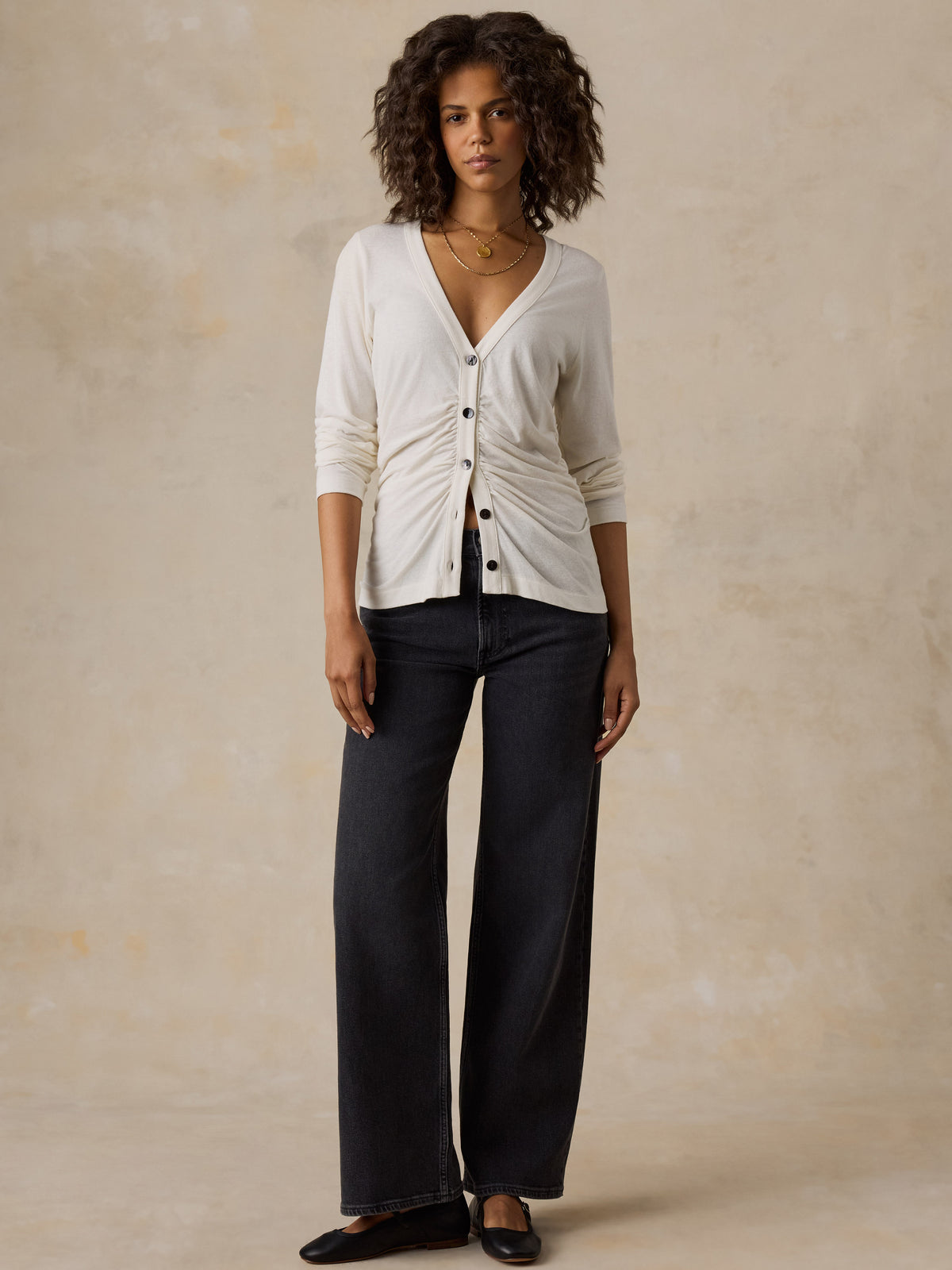 A woman wearing a white cardigan, black jeans, and black flats, image 2 of 6