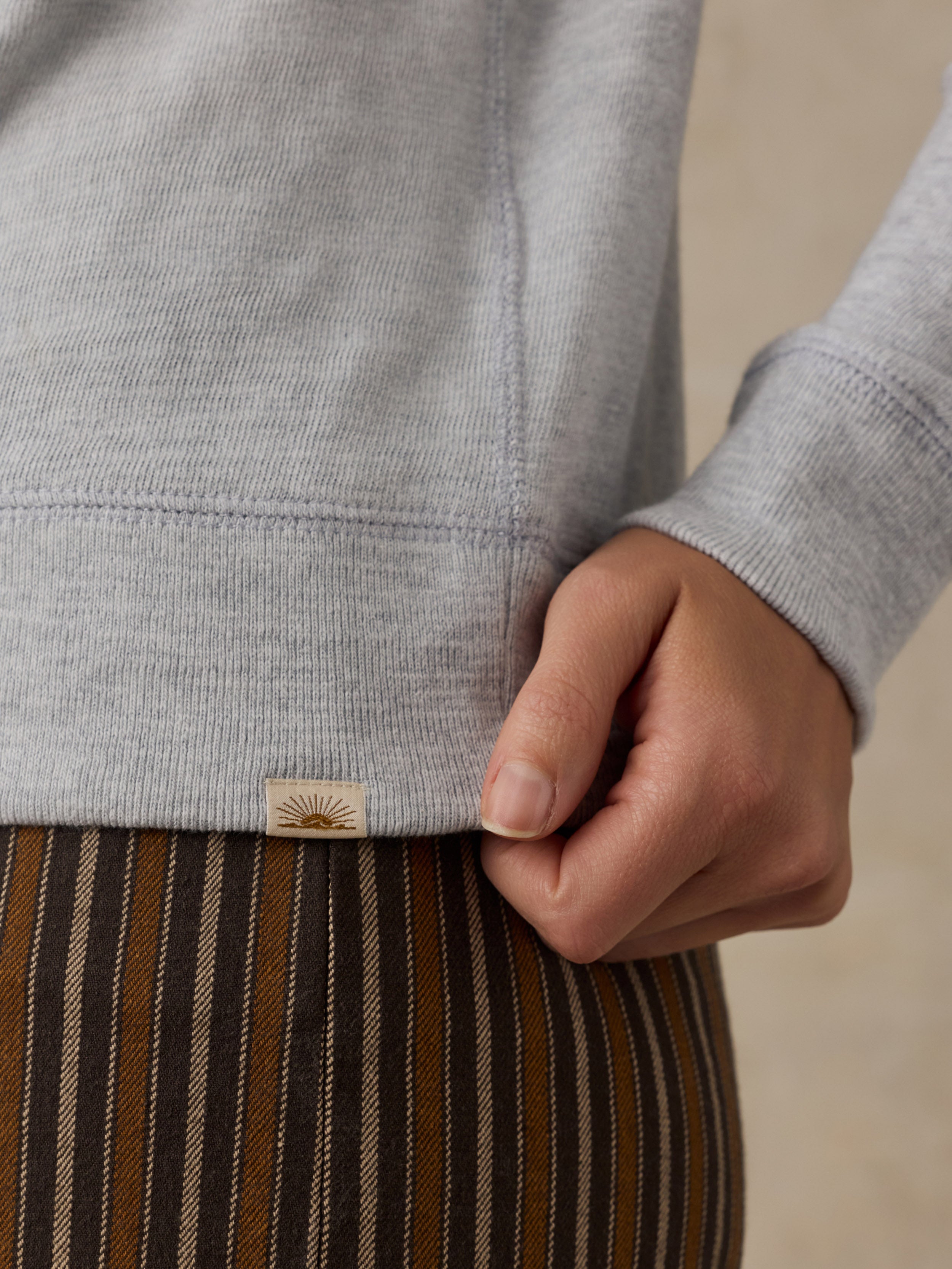 Close-up of a woman wearing a grey sweatshirt with a Faherty label at the hem and brown striped pants