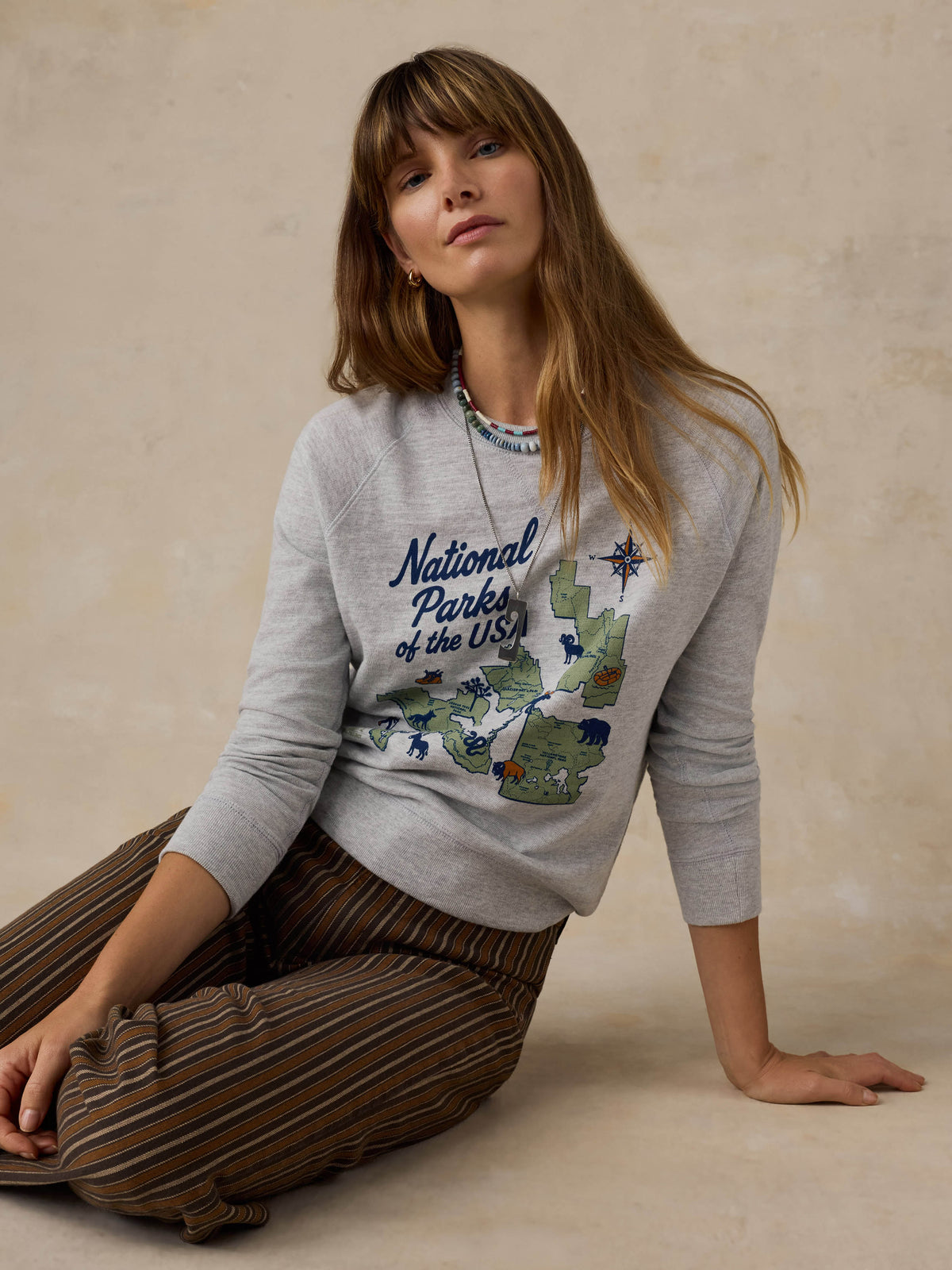 Woman wearing a grey crewneck with a National Parks graphic on the front against a beige background, image 3 of 7