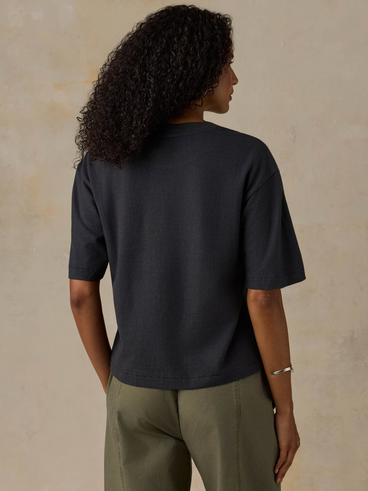 Woman wearing a black t-shirt and green pants against a beige background, image 4 of 6