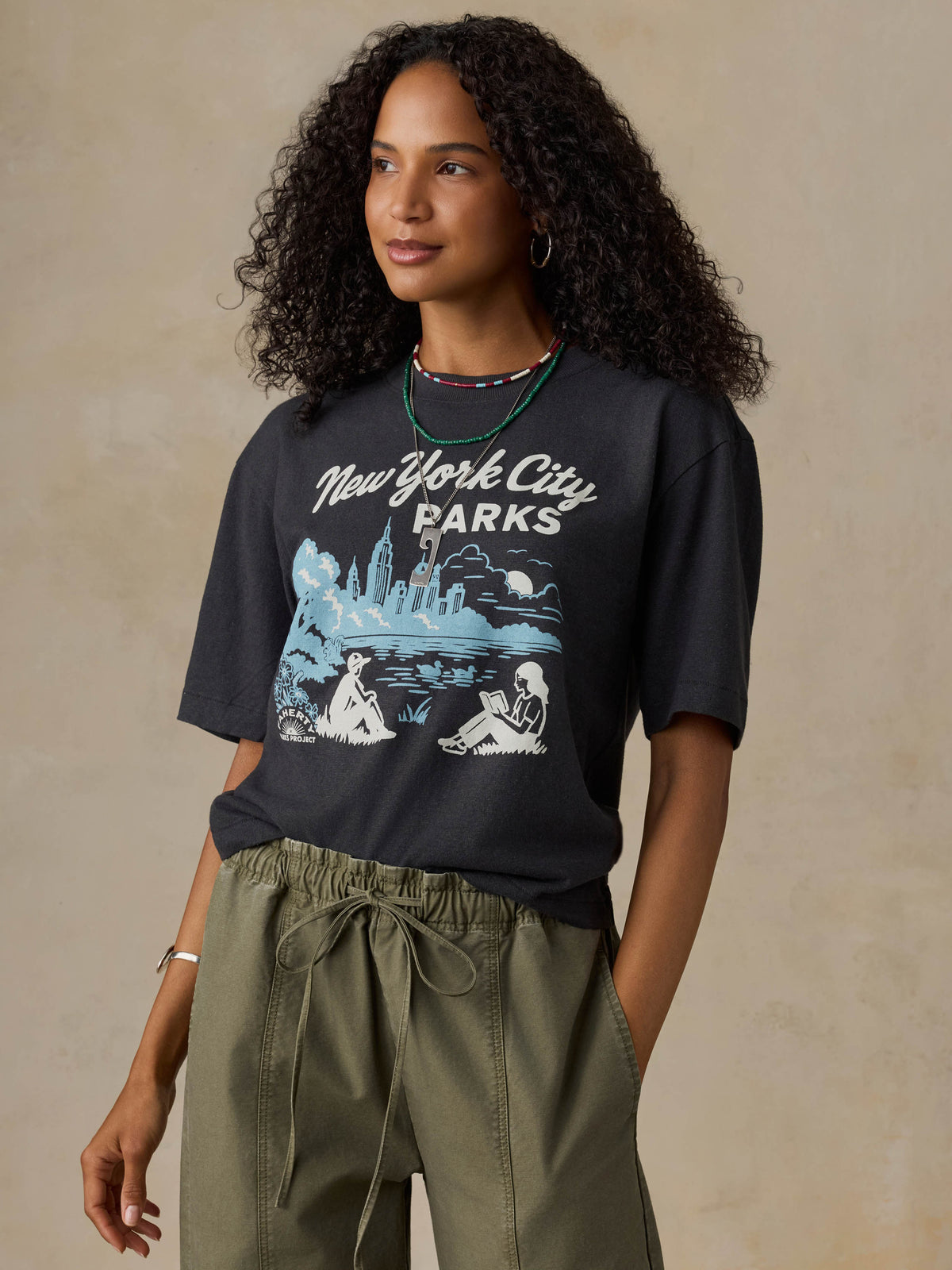 Woman wearing a black t-shirt with 'New York City Parks' graphic design on a beige background, image 2 of 6