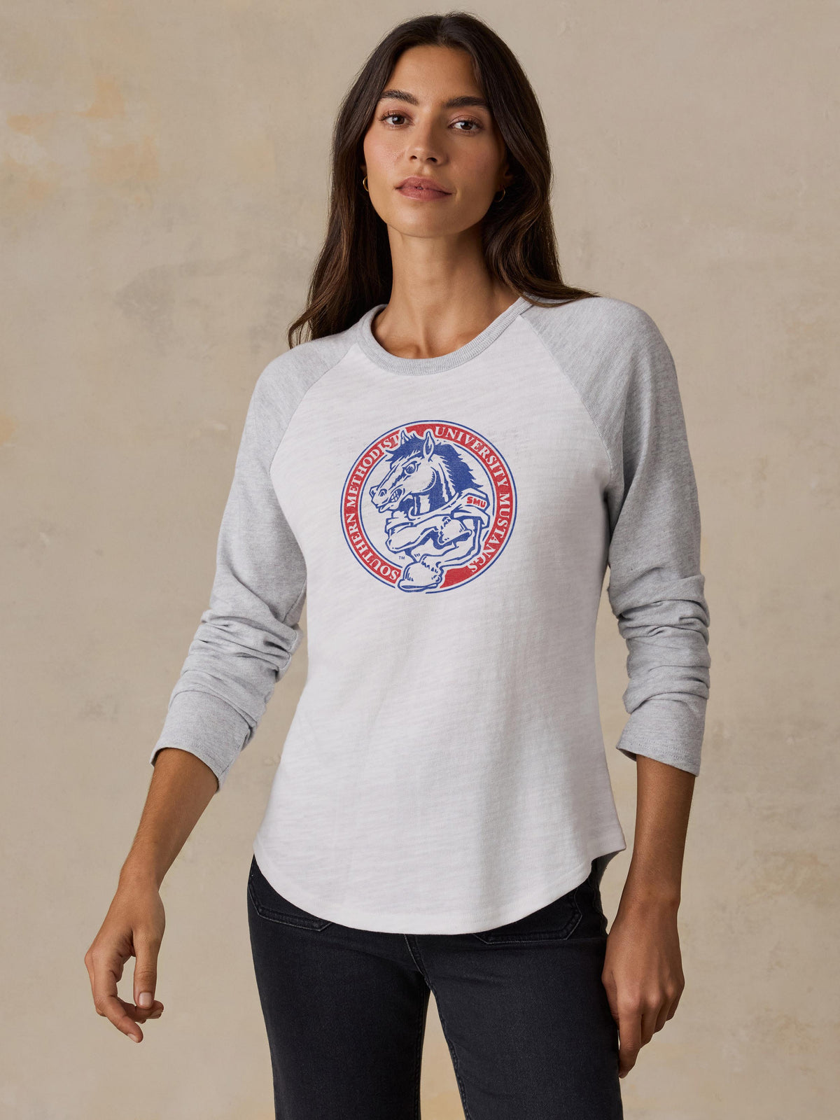 A woman wearing a white and grey SMU baseball tee and black jeans, image 1 of 2