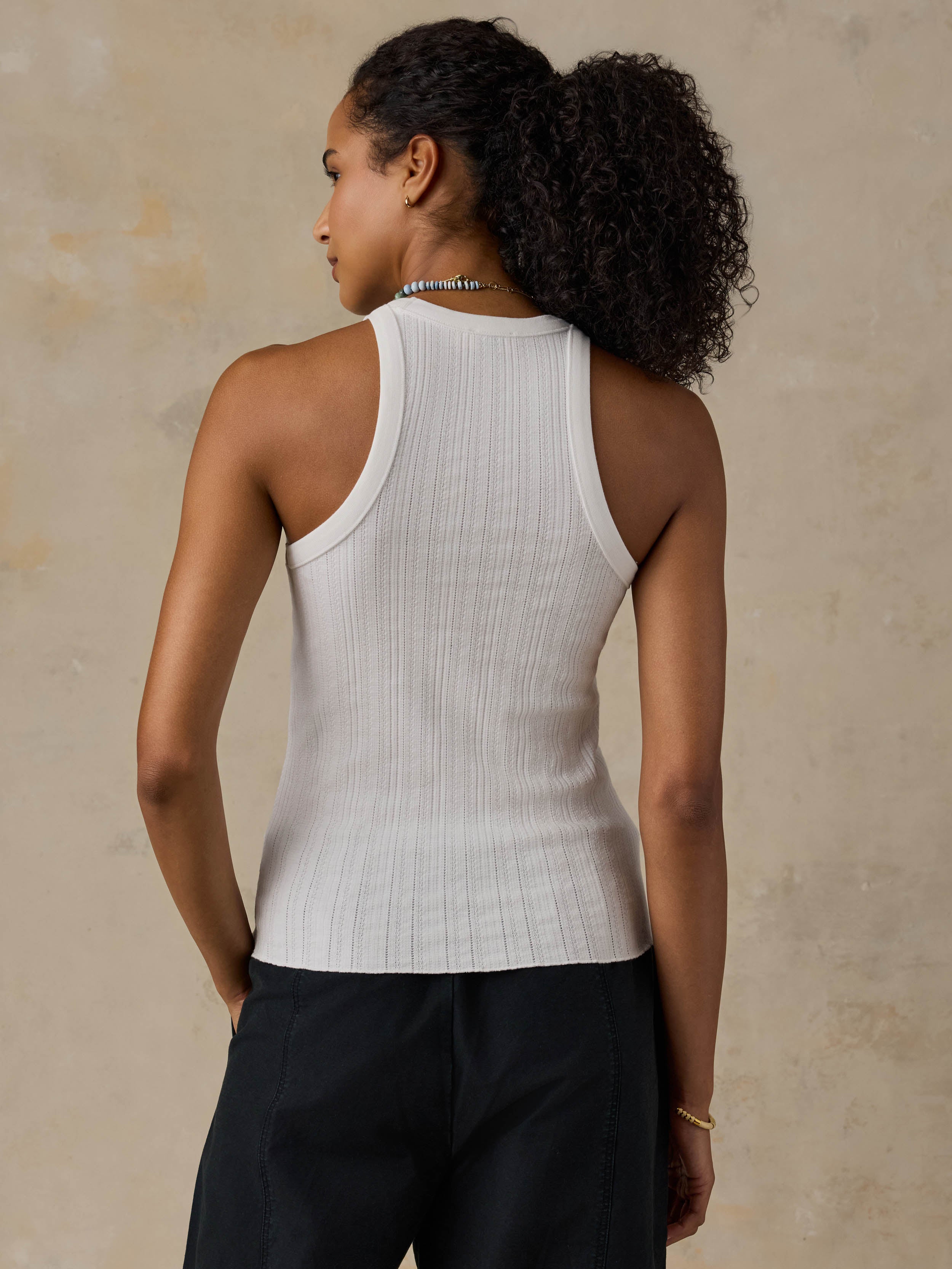 Woman wearing a white tank top and black pants against a beige background