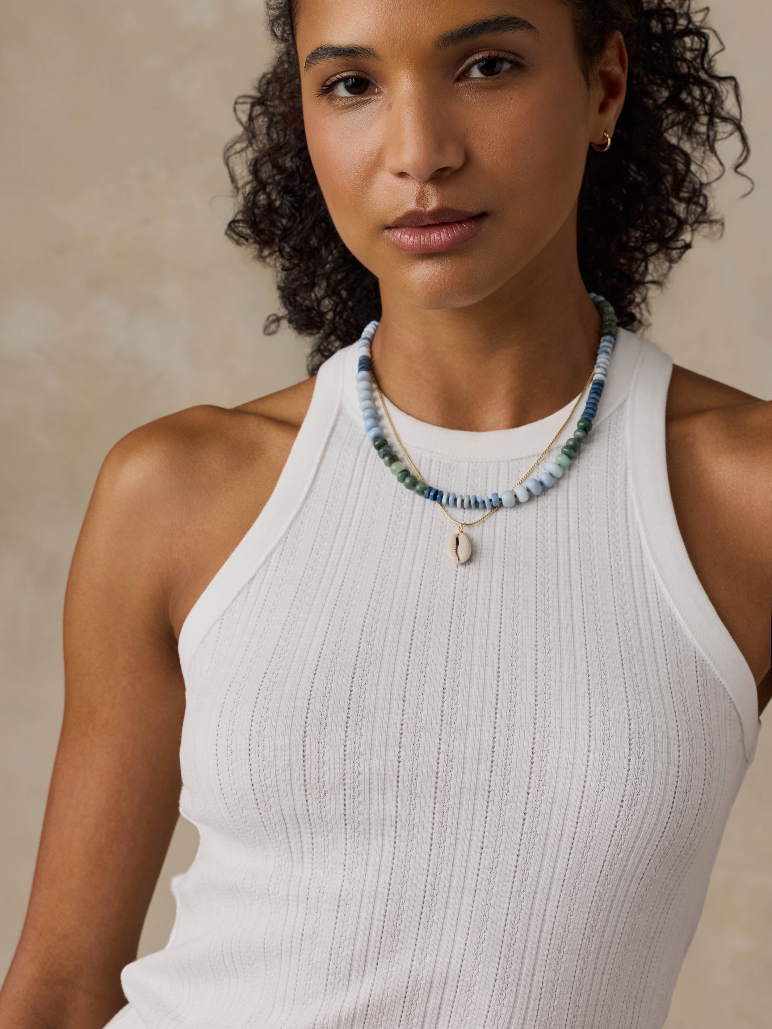 Woman wearing a white tank top against a beige background