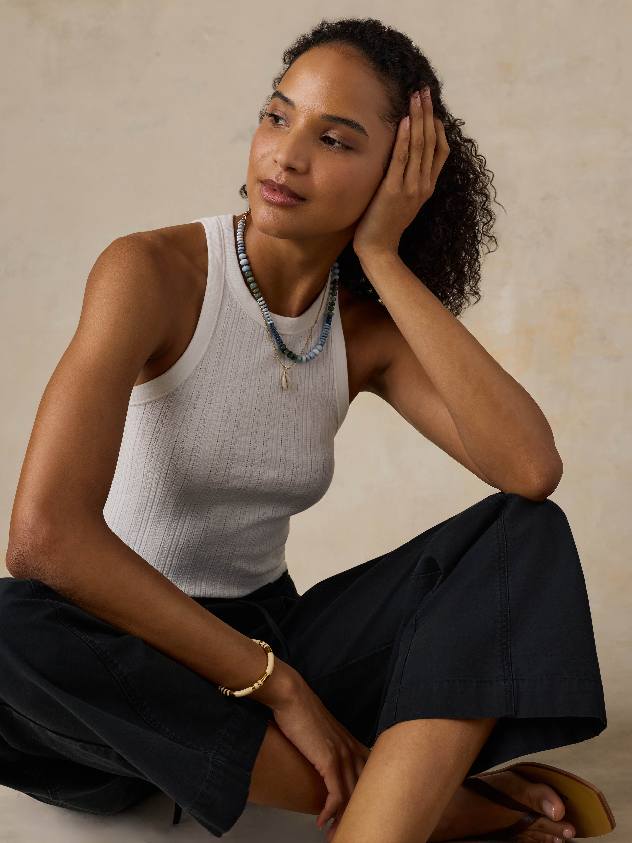 Woman wearing a white tank top and black pants against a beige background