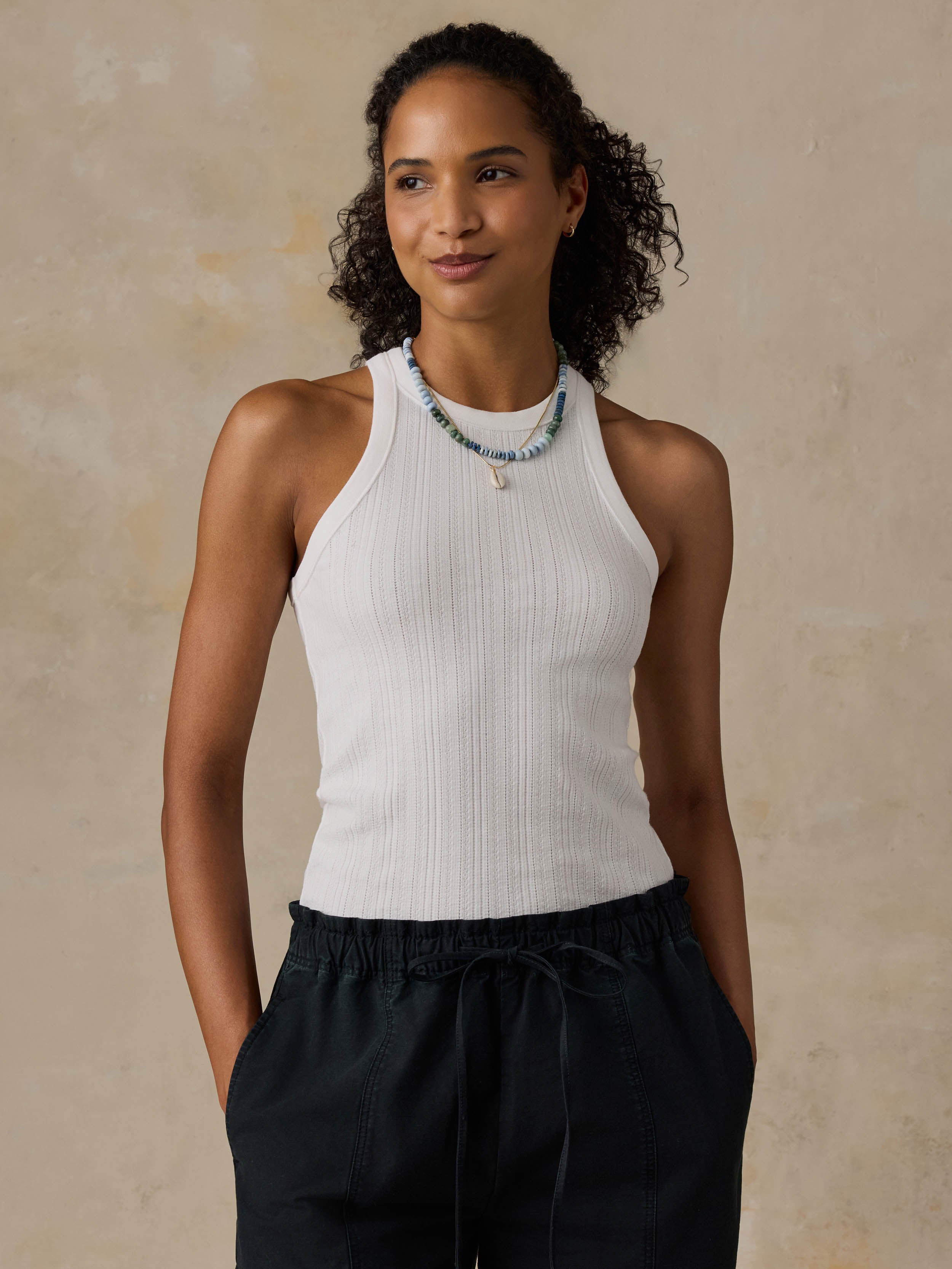 Woman wearing a white tank top and black pants against a beige background