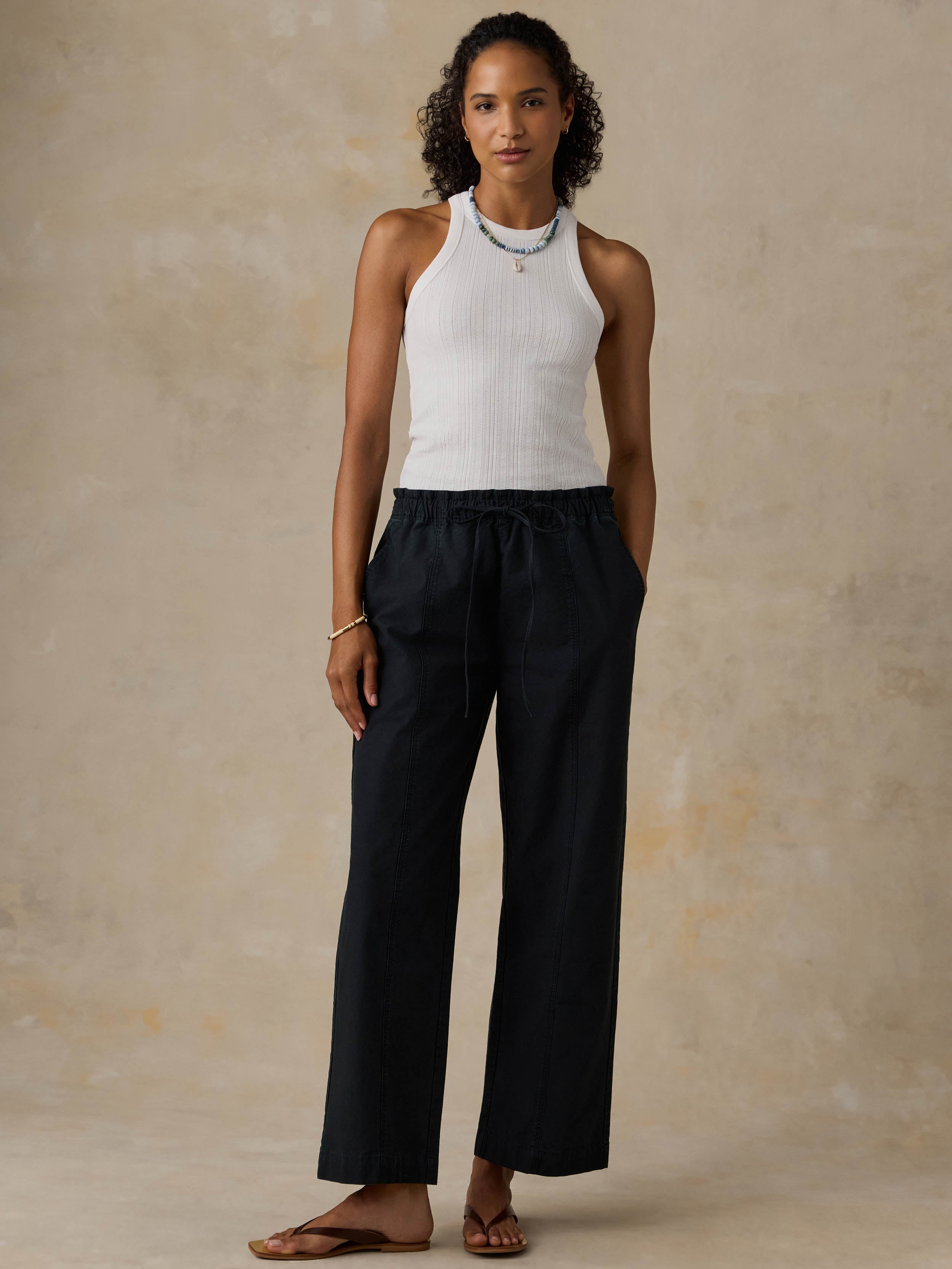 Woman wearing a white tank top and black pants against a beige background