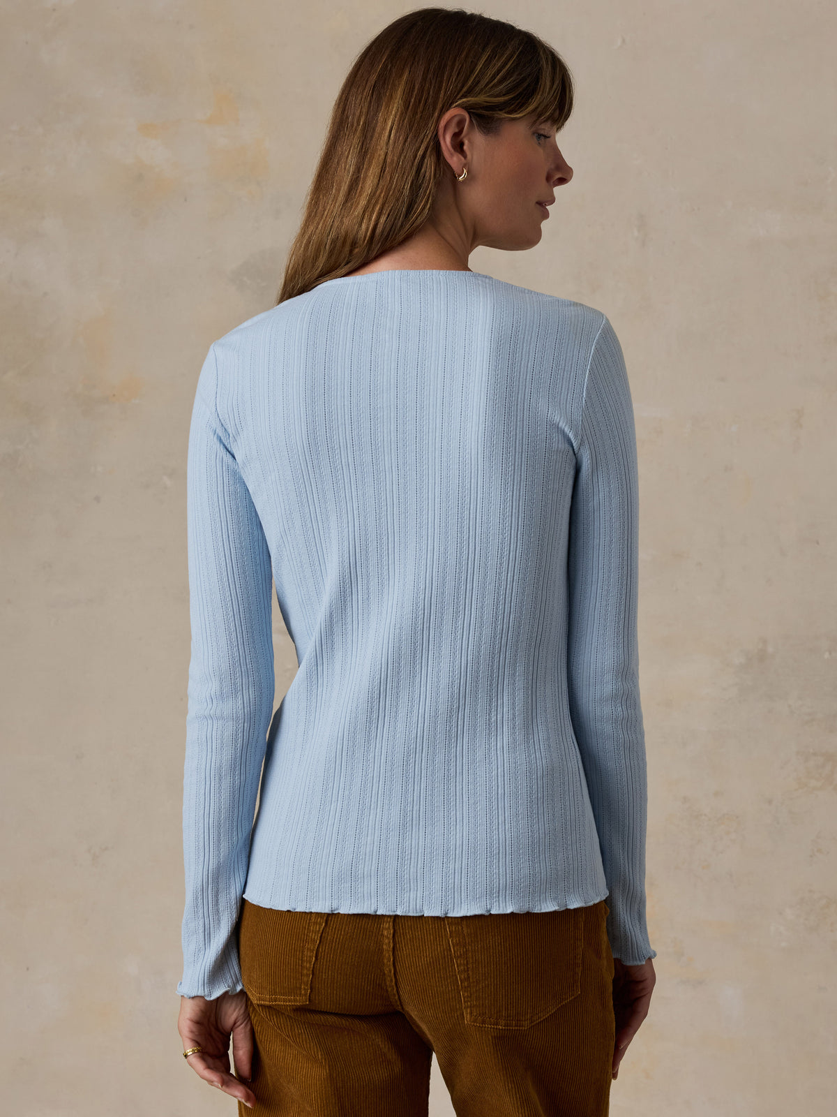 A woman viewed from behind wearing a light blue cardigan and brown corduroy pants, image 3 of 6