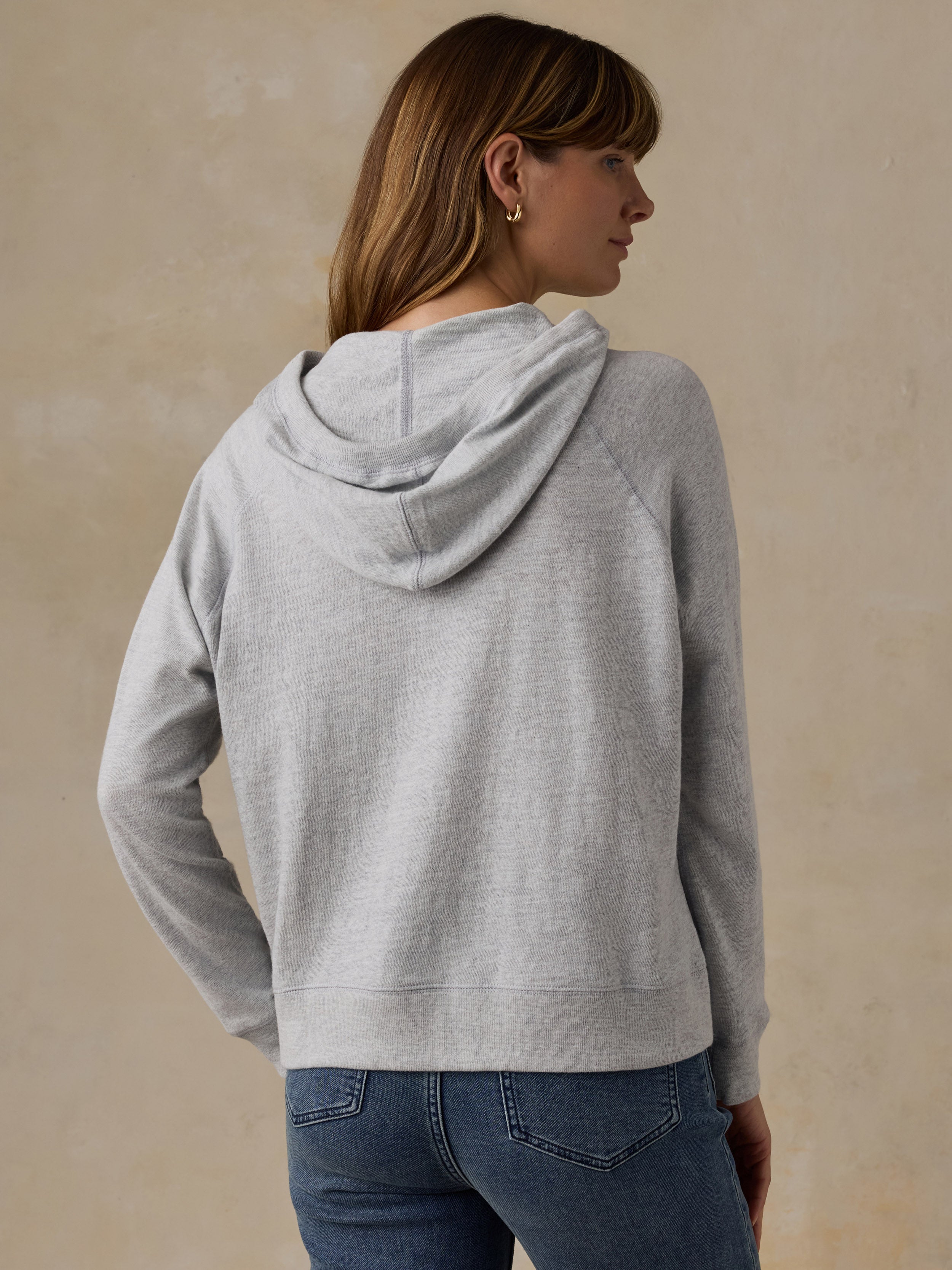Woman wearing a grey sweatshirt and blue jeans against a beige background