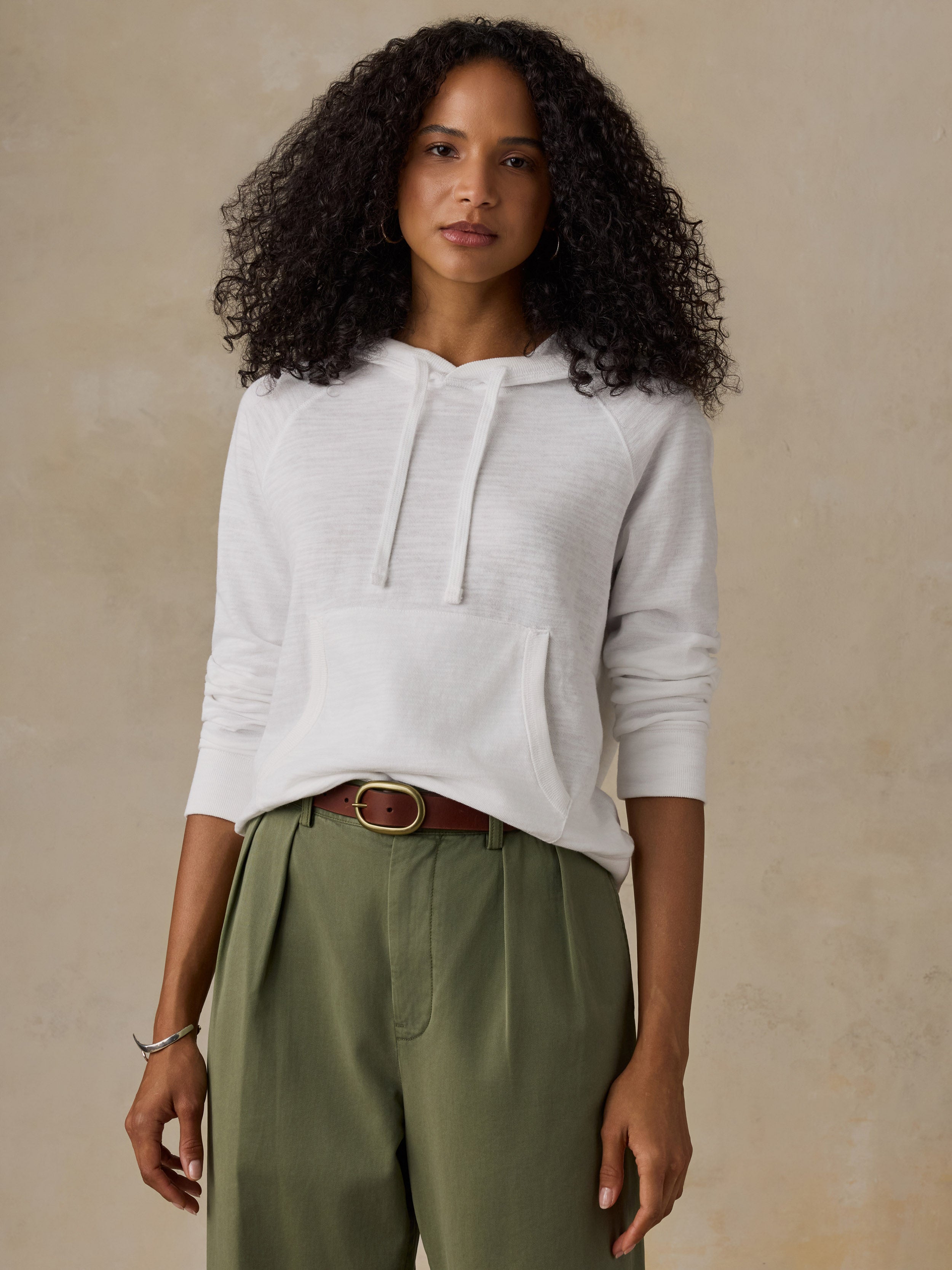 Woman wearing a white hoodie and olive green pants against a beige background
