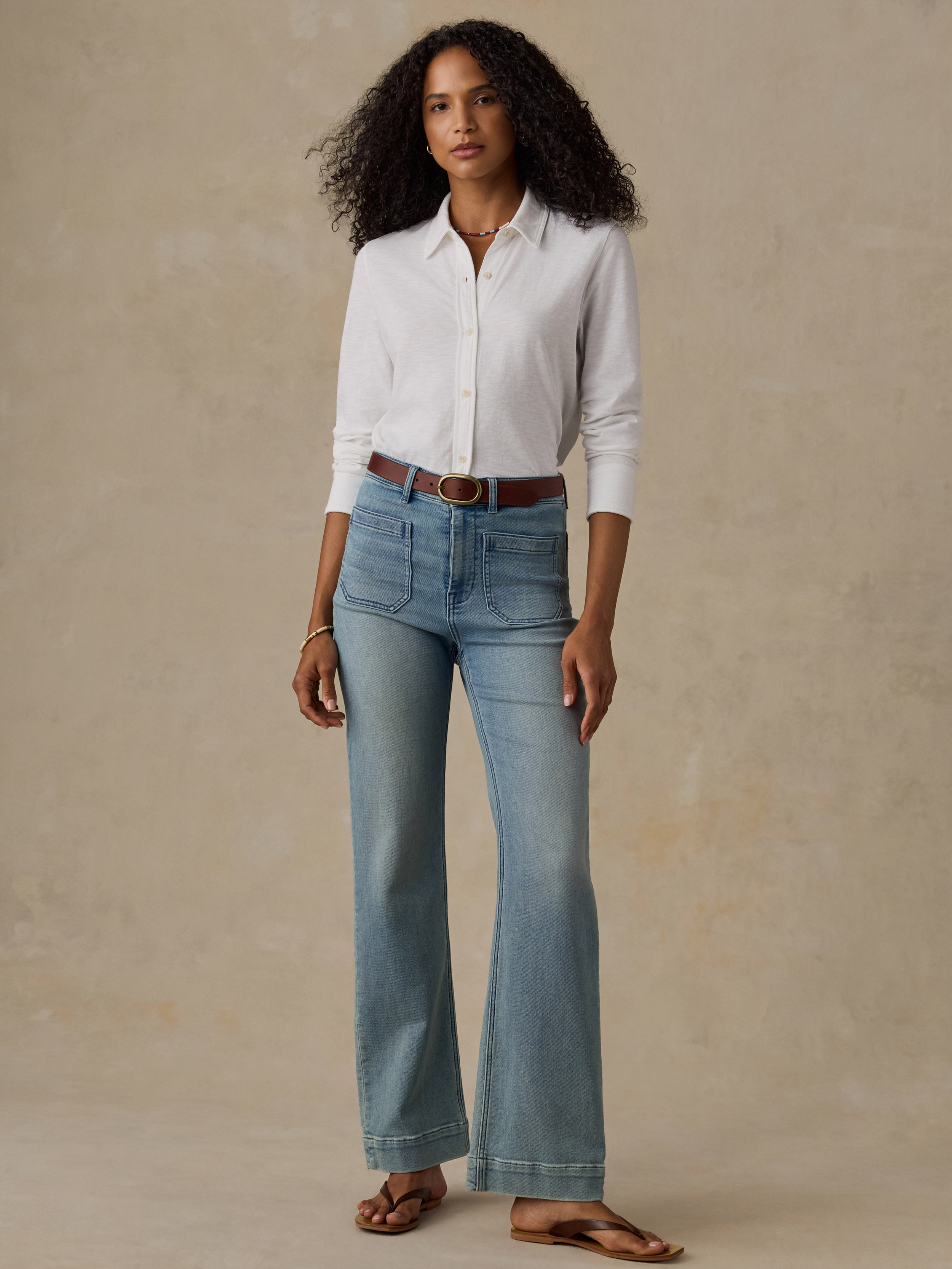 Woman wearing a white button down shirt and blue jeans against a beige background
