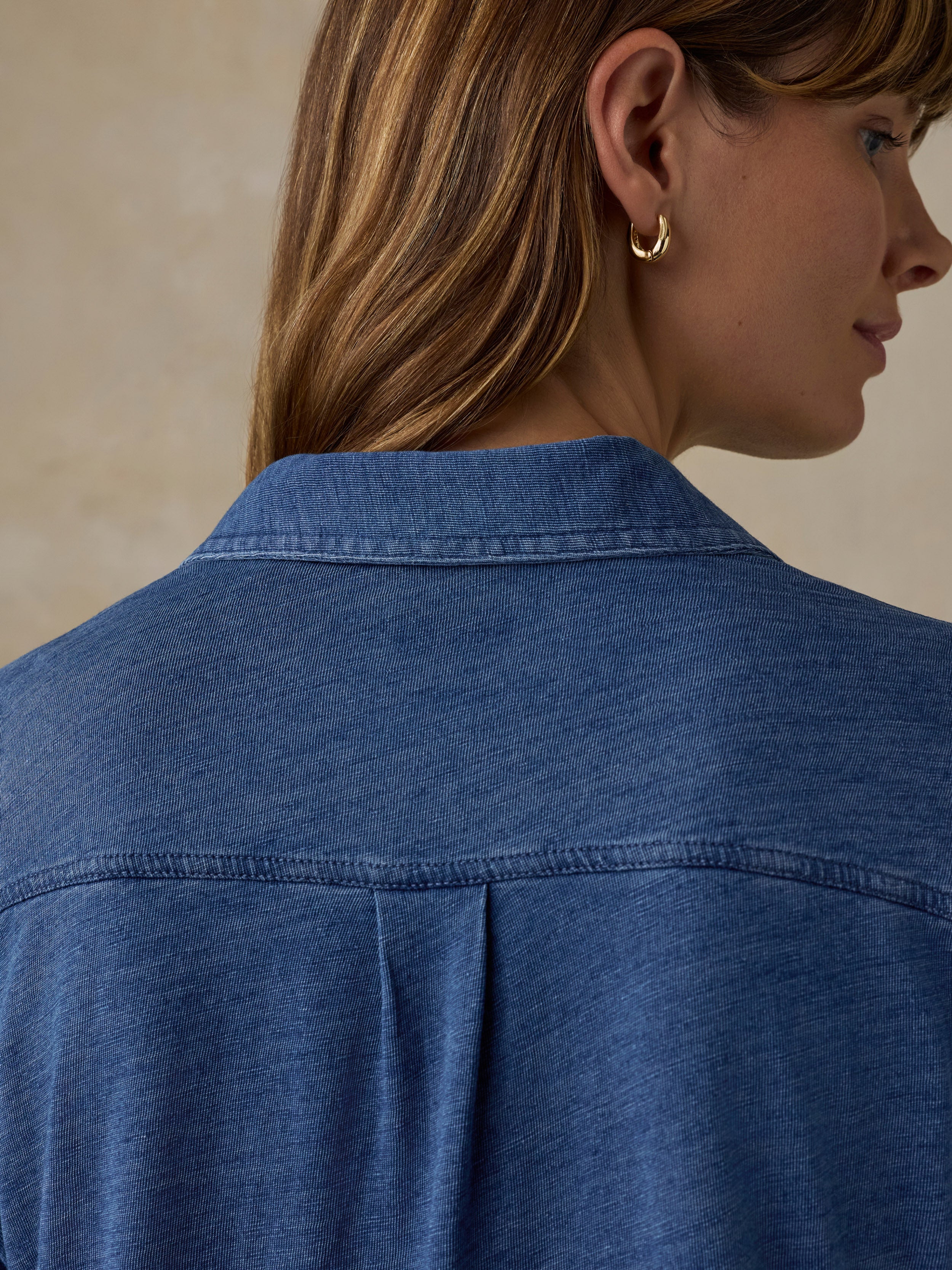 Woman wearing a blue button down shirt against a beige background