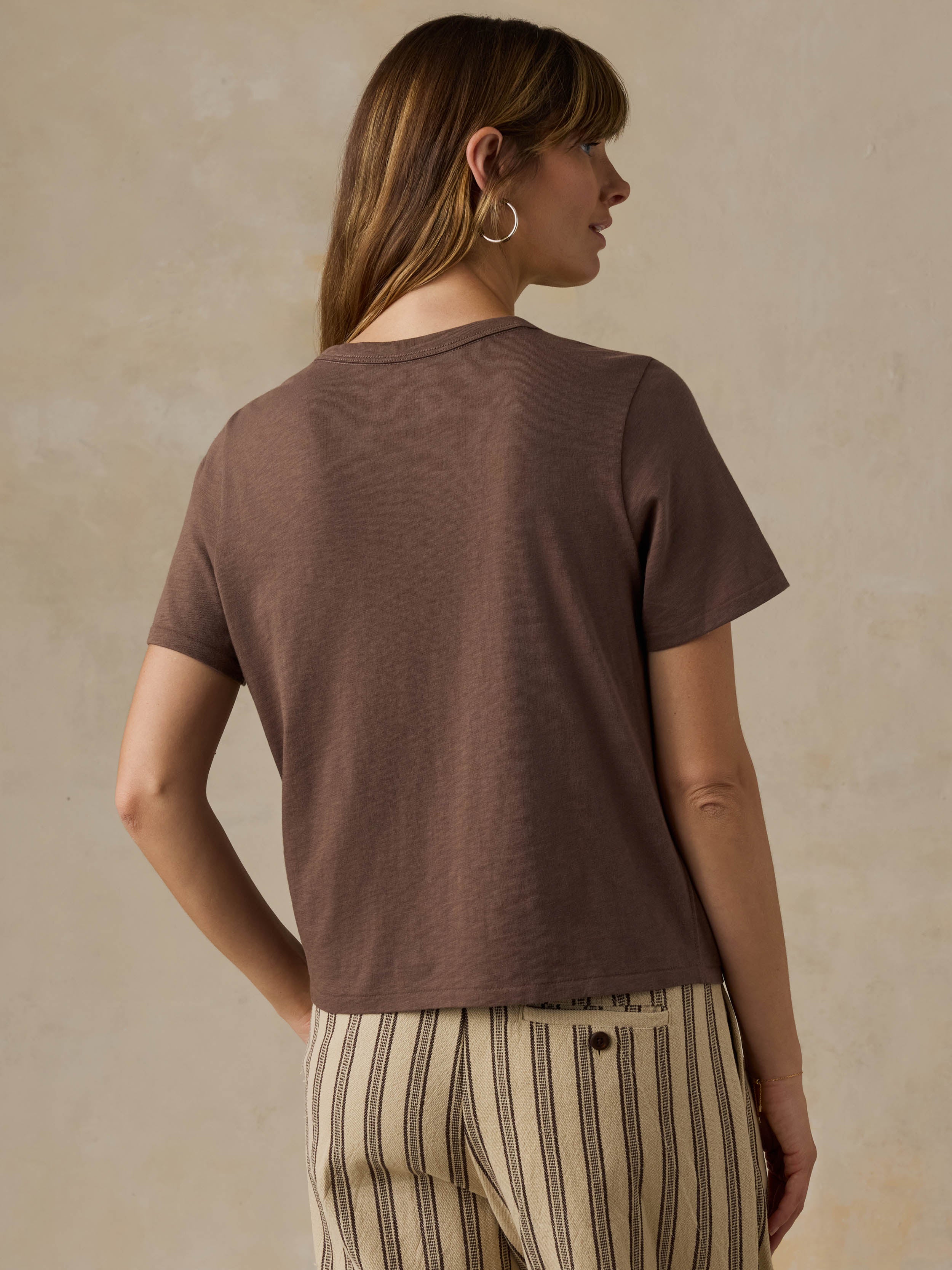 Woman wearing a brown t-shirt and striped pants against a beige background