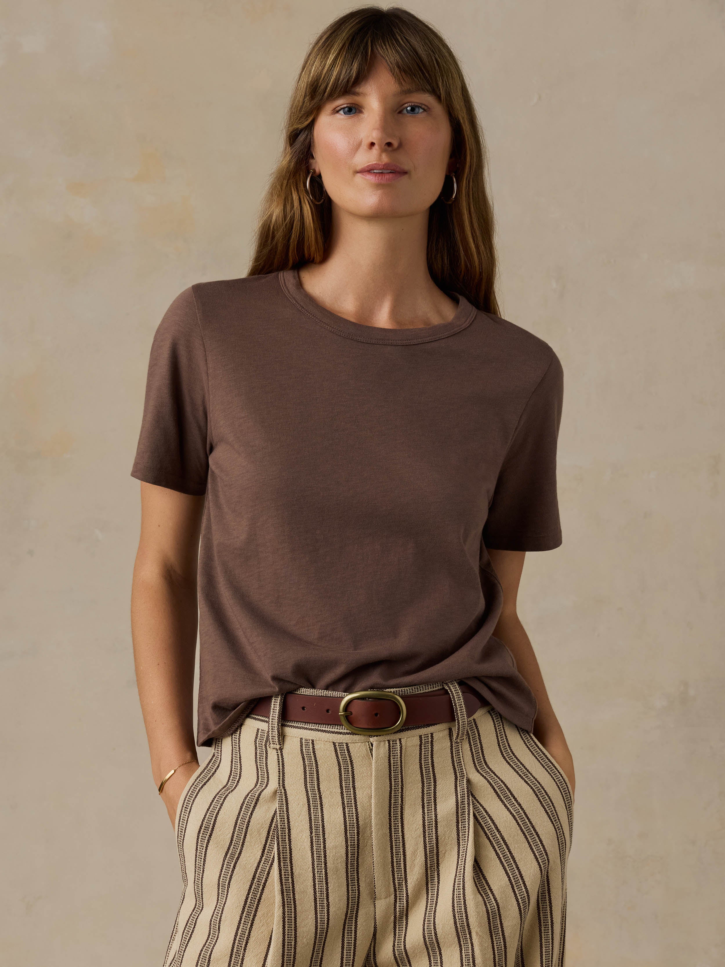 Woman wearing a brown t-shirt and striped pants against a beige background