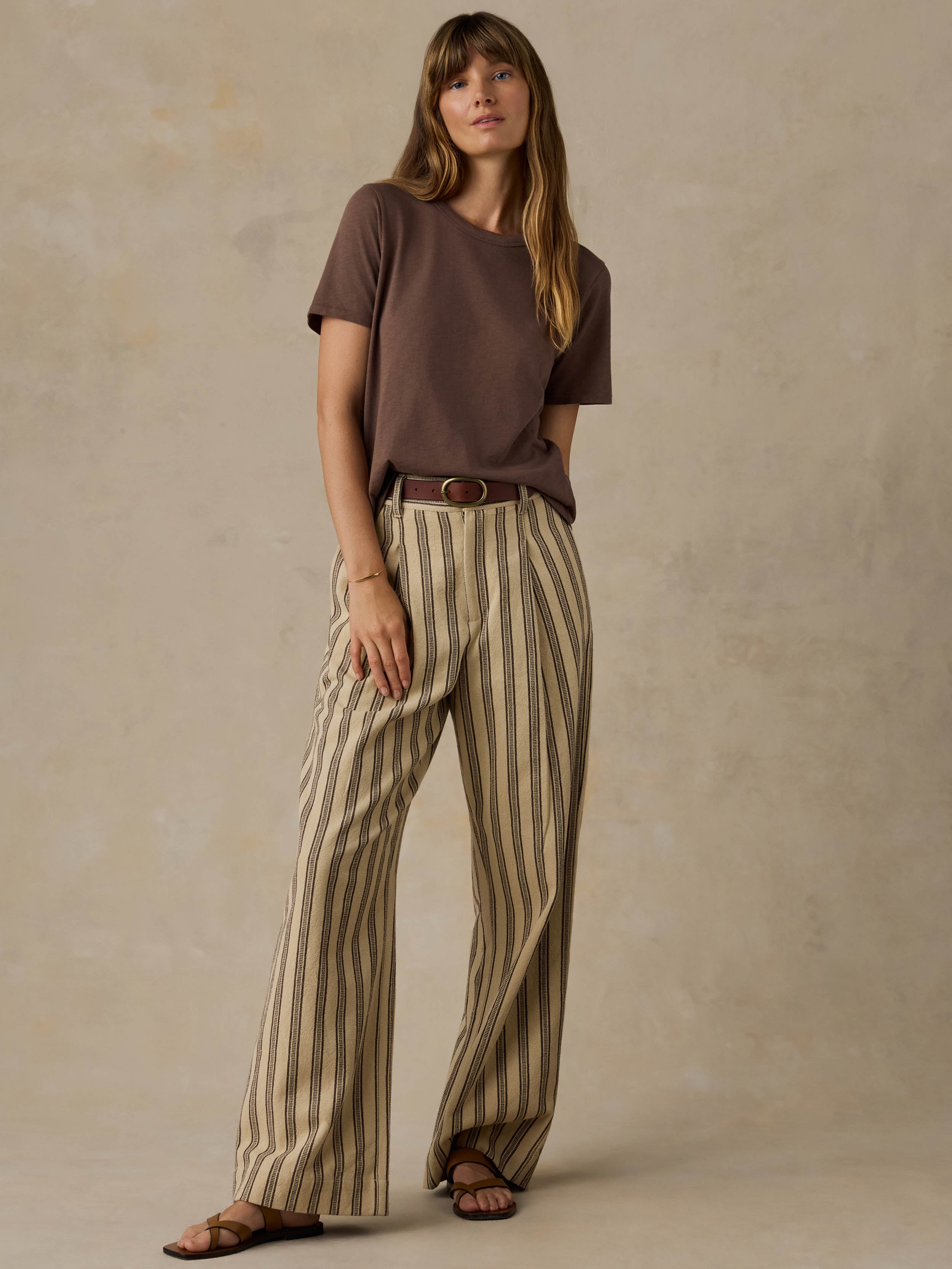 Woman wearing a brown t-shirt and striped pants against a beige background
