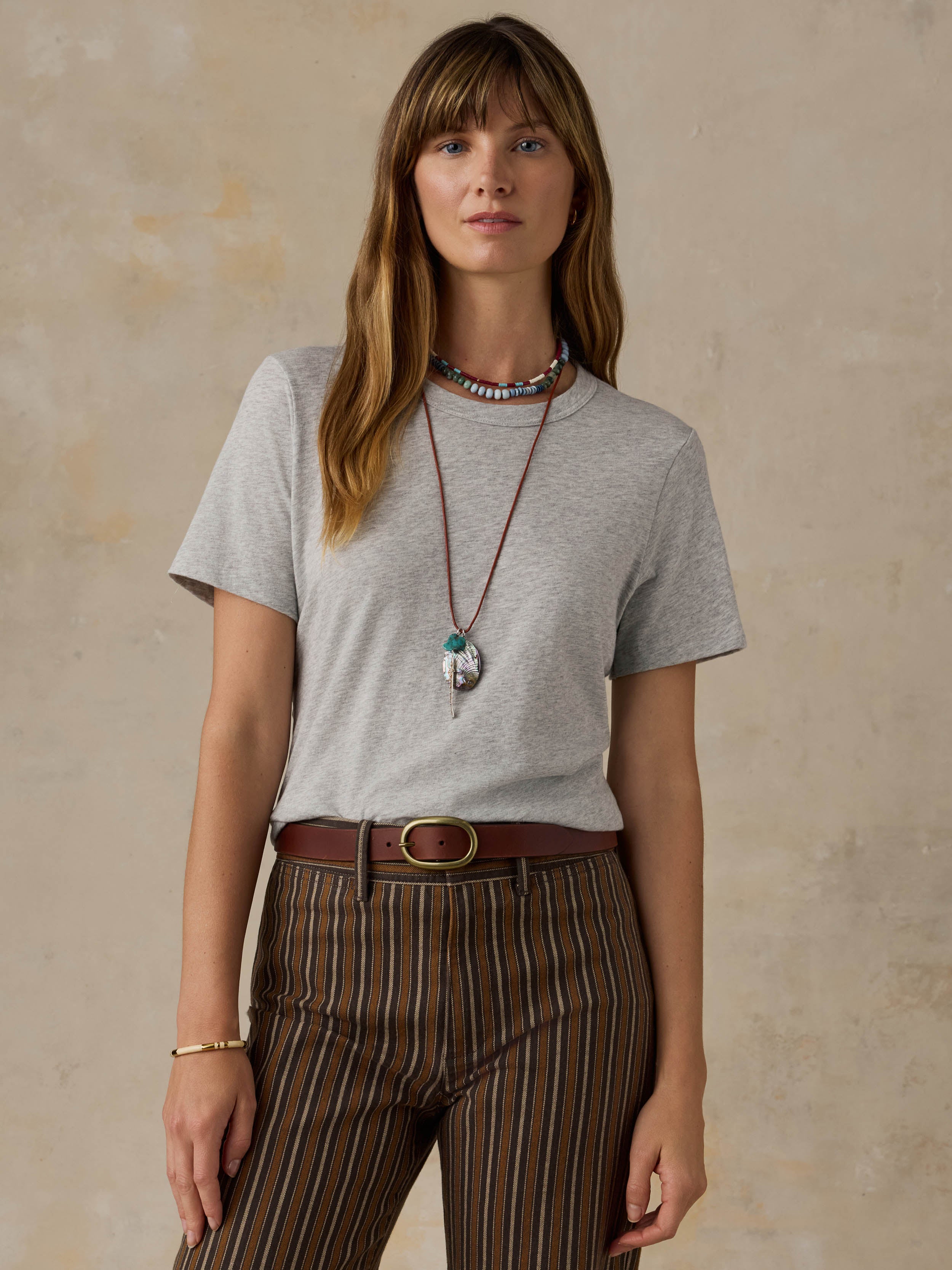 A woman wearing a grey t-shirt and striped pants against a beige background