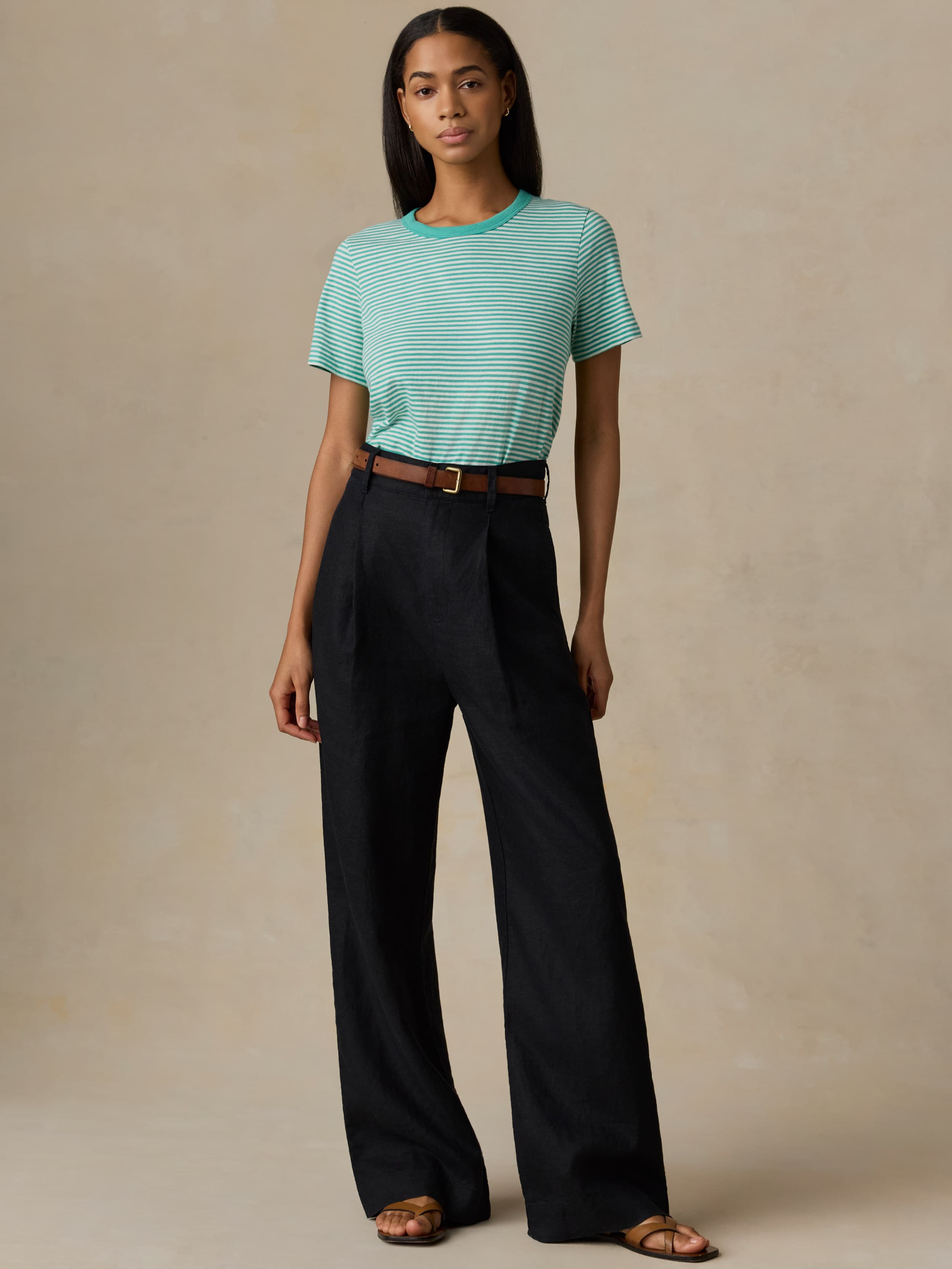 Woman wearing a green striped shirt and black pants against a beige background