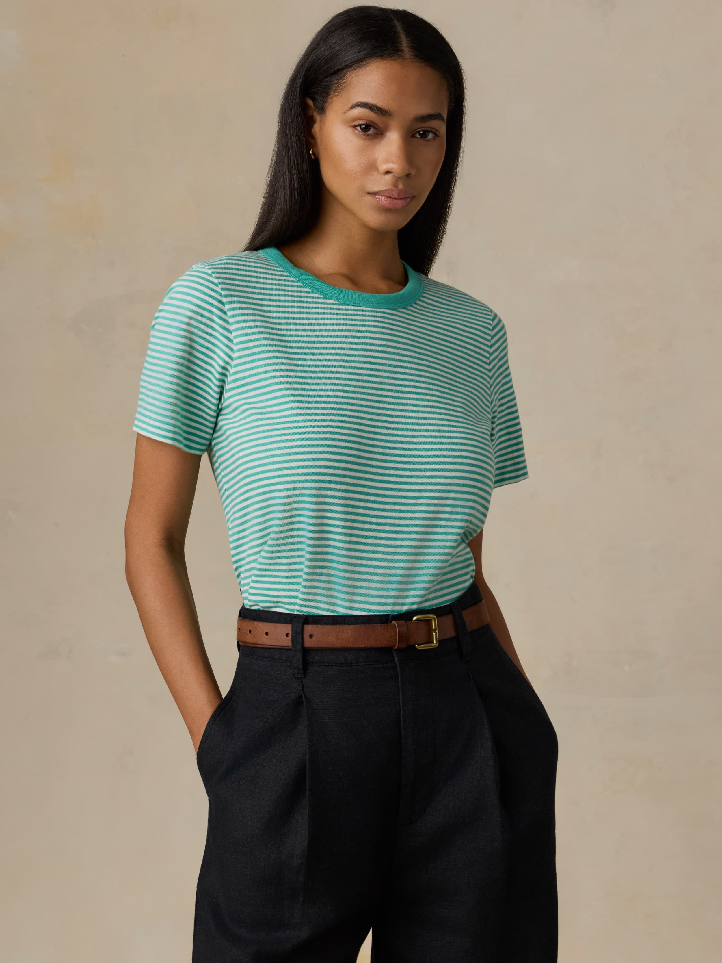 Woman wearing a green striped shirt and black pants against a beige background