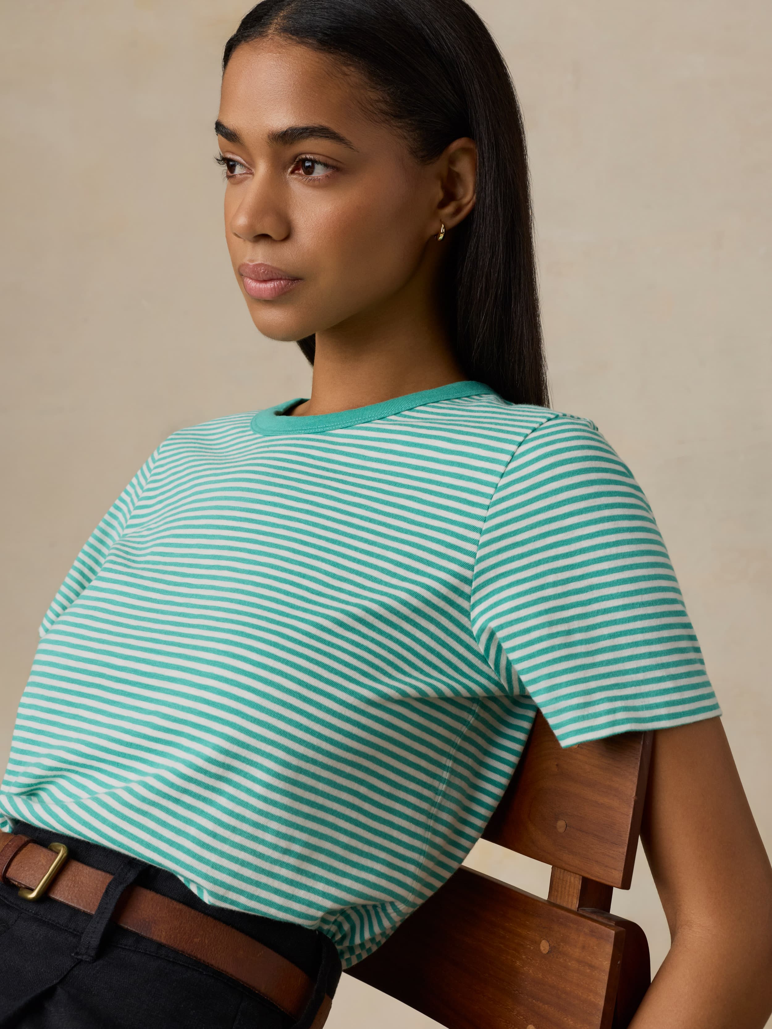 Woman wearing a green and white striped shirt sitting on a wooden chair against a beige background