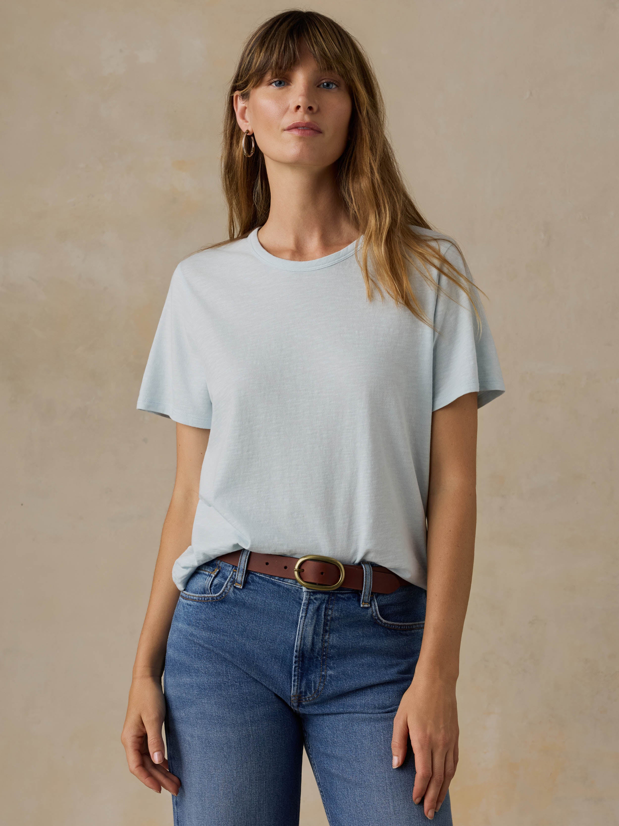 Woman wearing a light blue t-shirt and blue jeans against a beige background