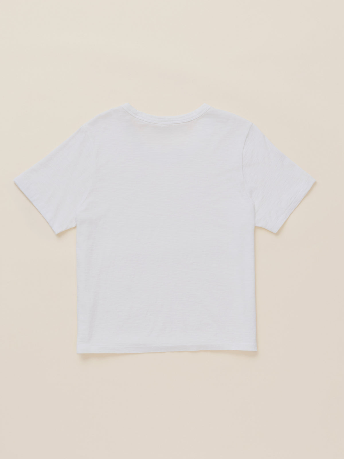 A plain white short-sleeve crop top t-shirt shown from the back, laid flat on a light beige background., image 7 of 7