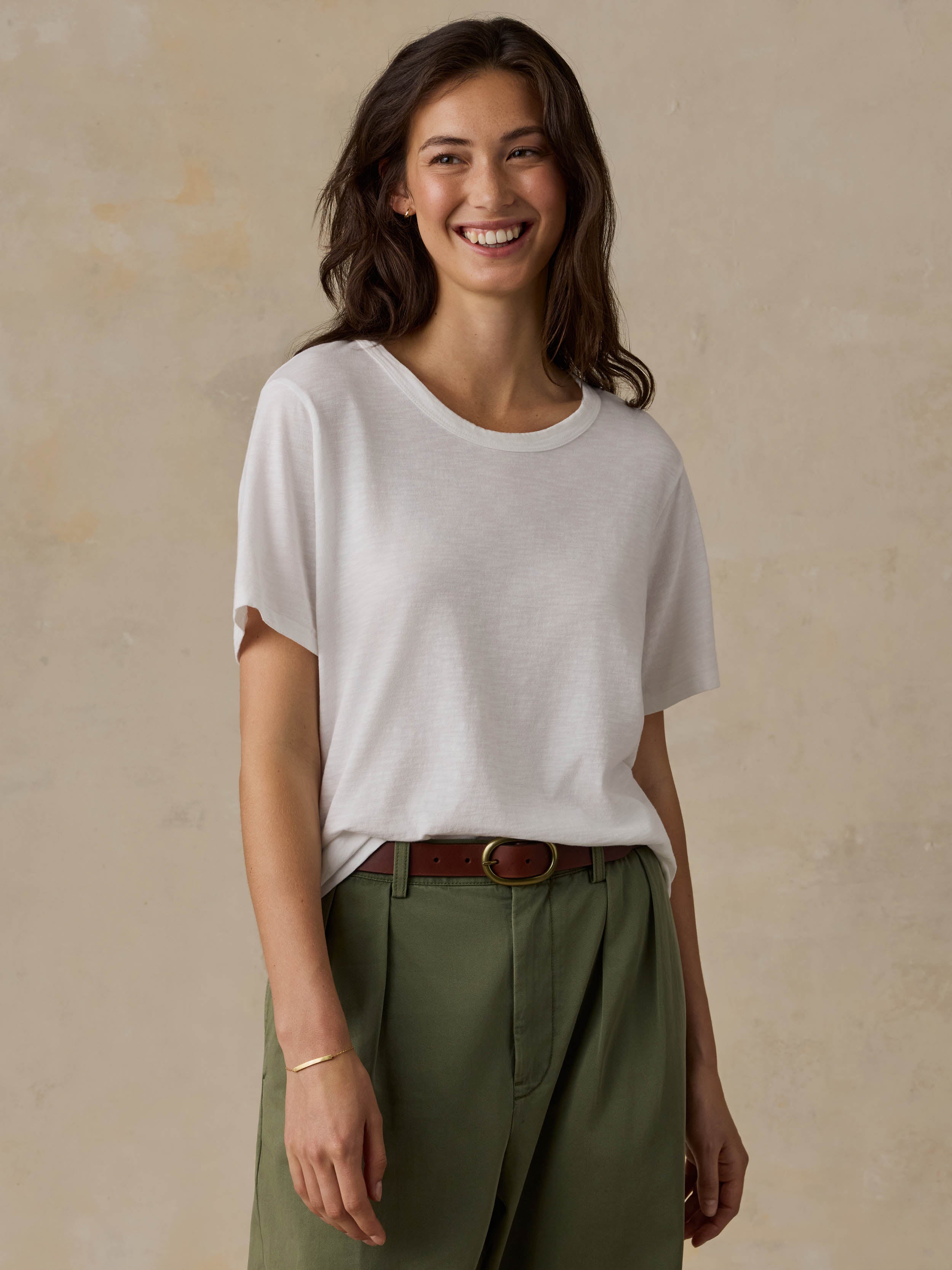 Woman wearing a white t-shirt and green pants against a beige background