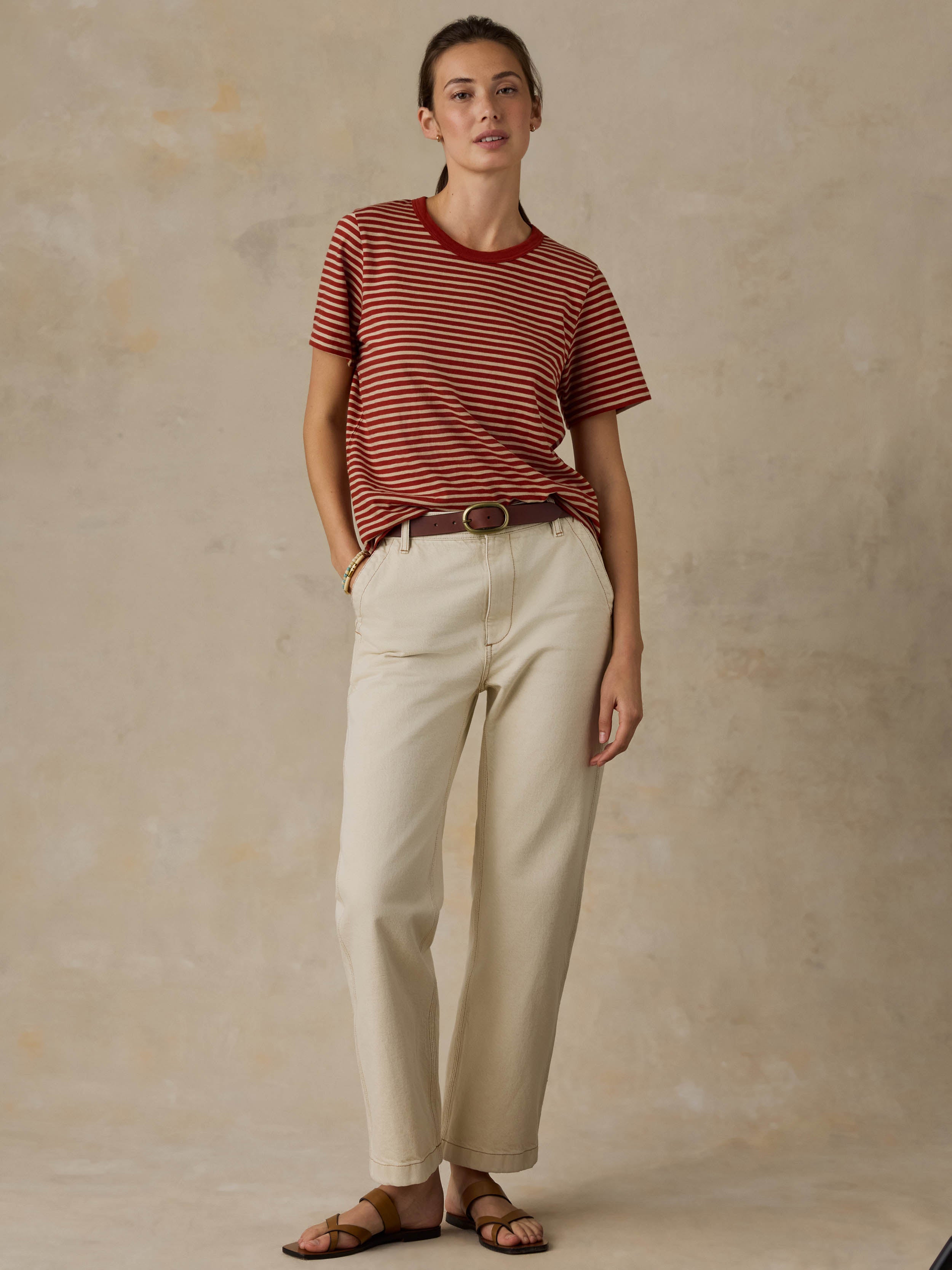Woman wearing a red striped shirt and beige pants against a beige background