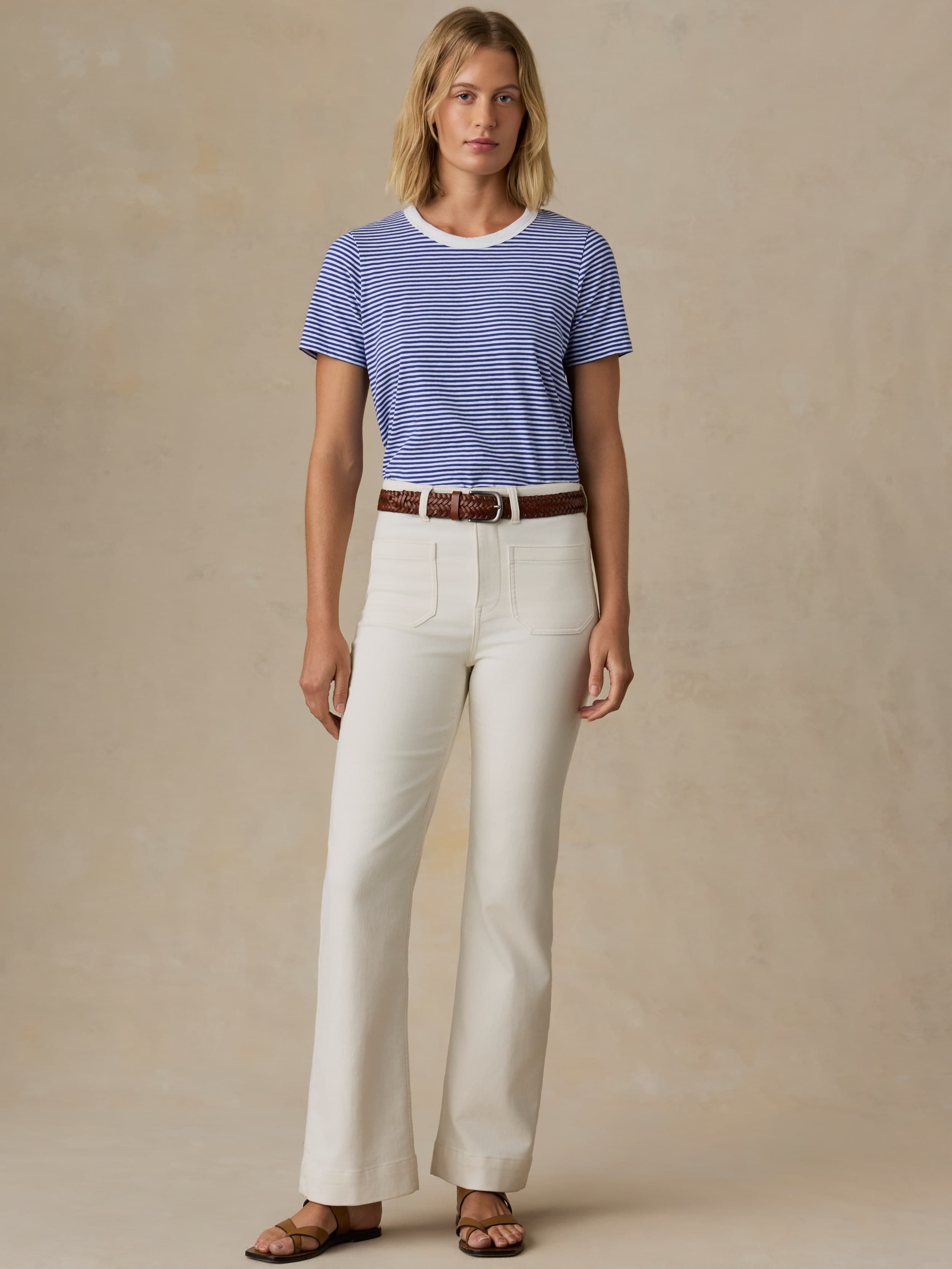 Woman wearing a blue and white striped shirt and white pants against a beige background