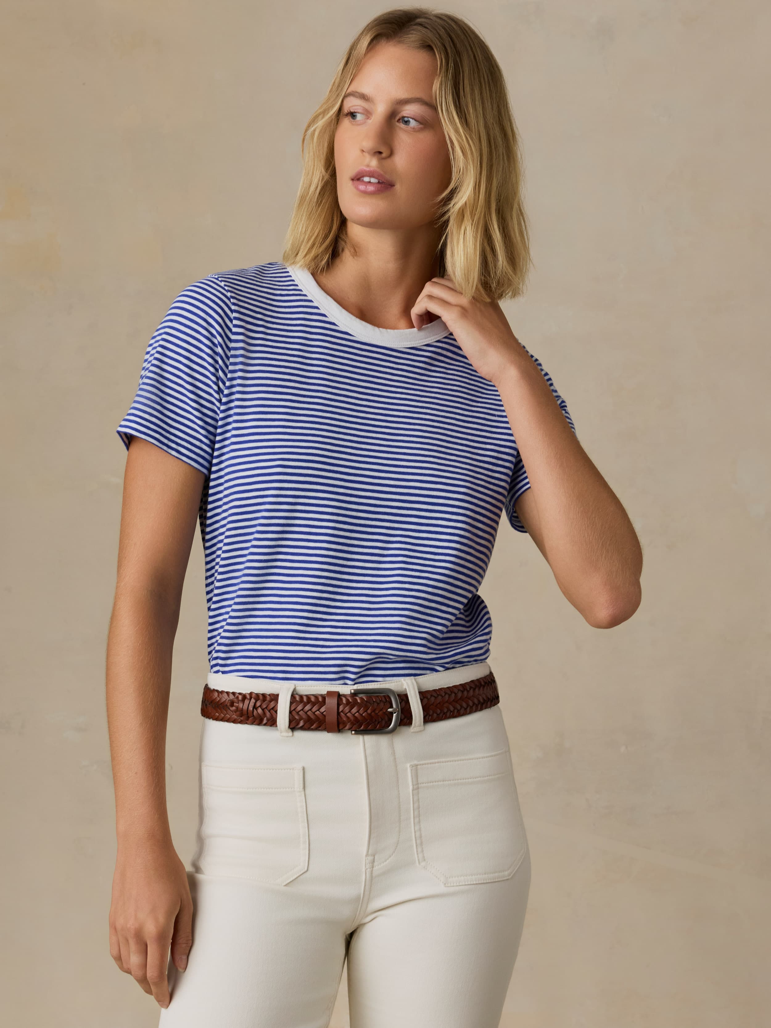 Woman wearing a blue and white striped shirt with white pants on a beige background