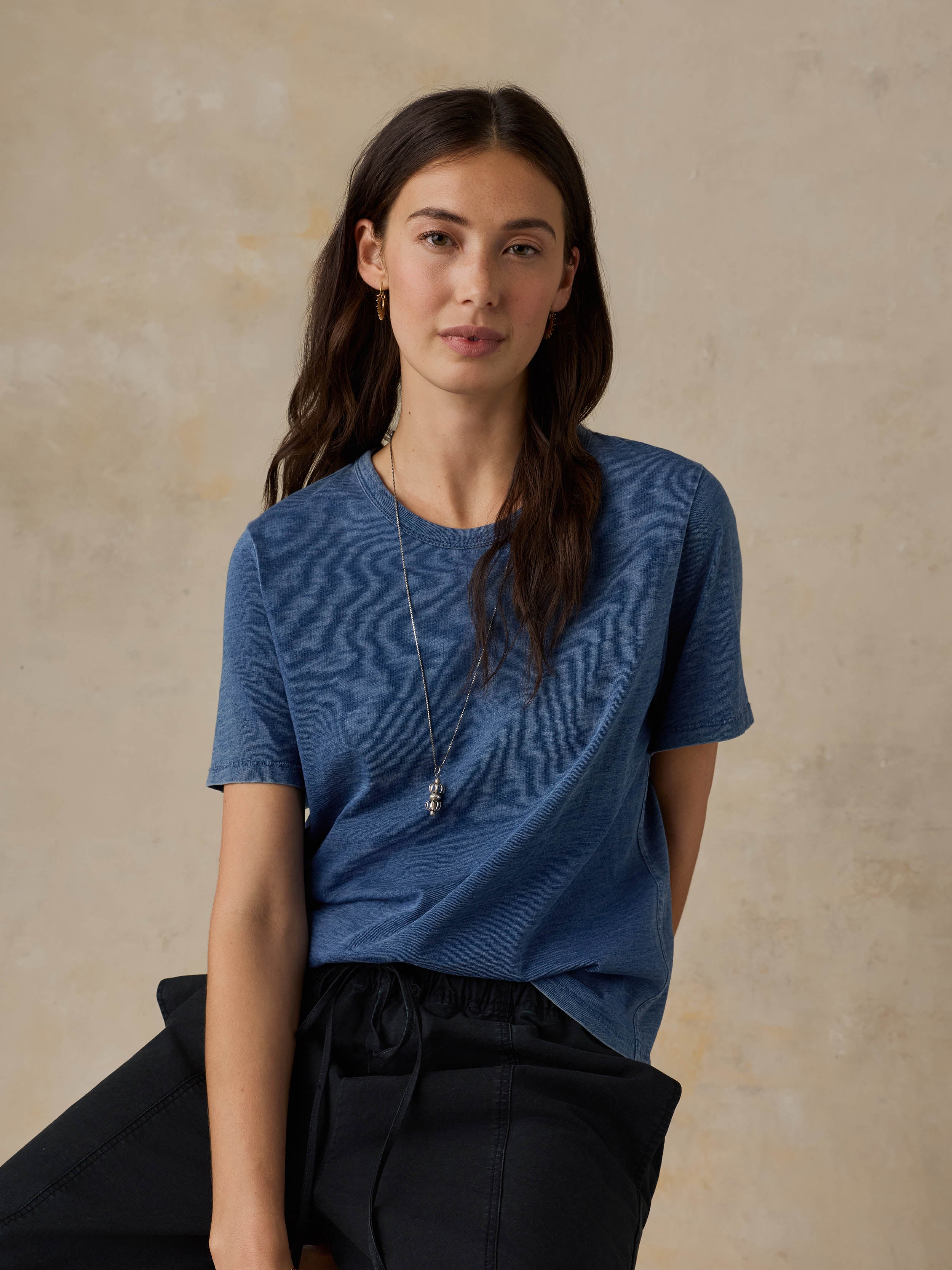 Woman wearing a blue t-shirt and black pants against a beige background