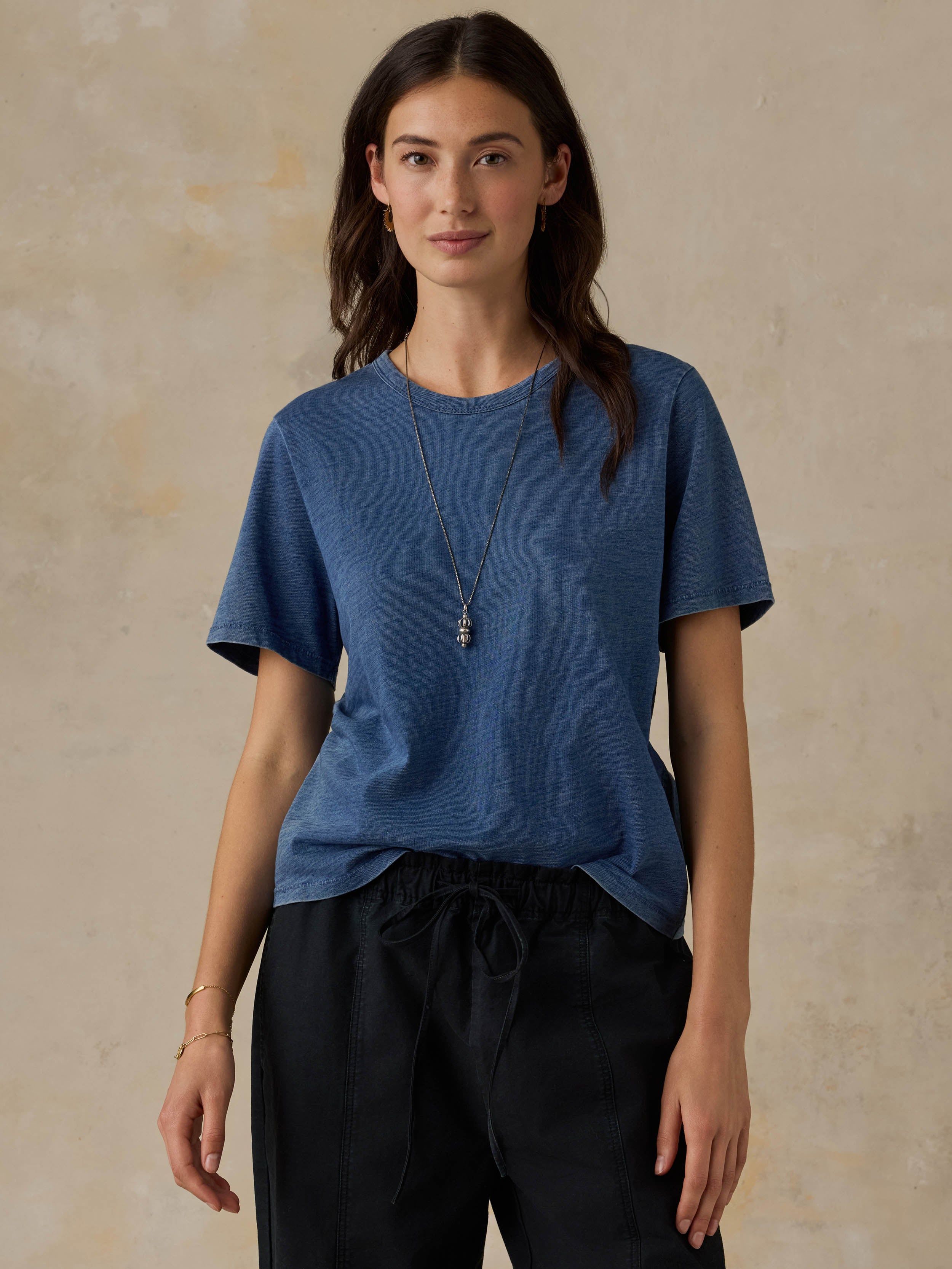 Woman wearing a blue t-shirt and black pants against a beige background