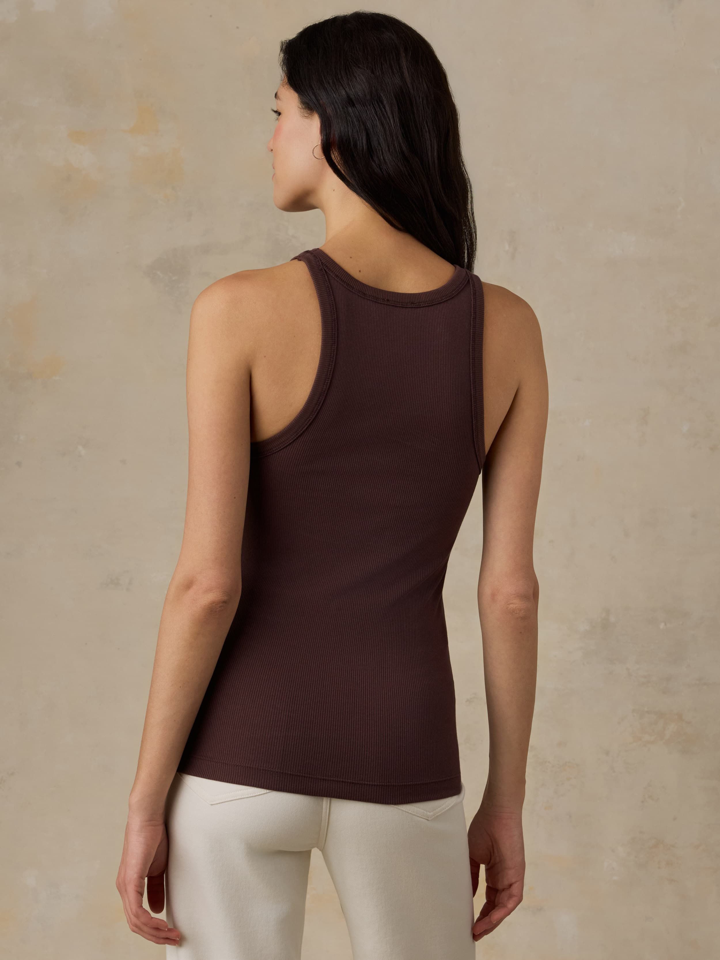 Woman wearing a brown tank top and white jeans against a beige background