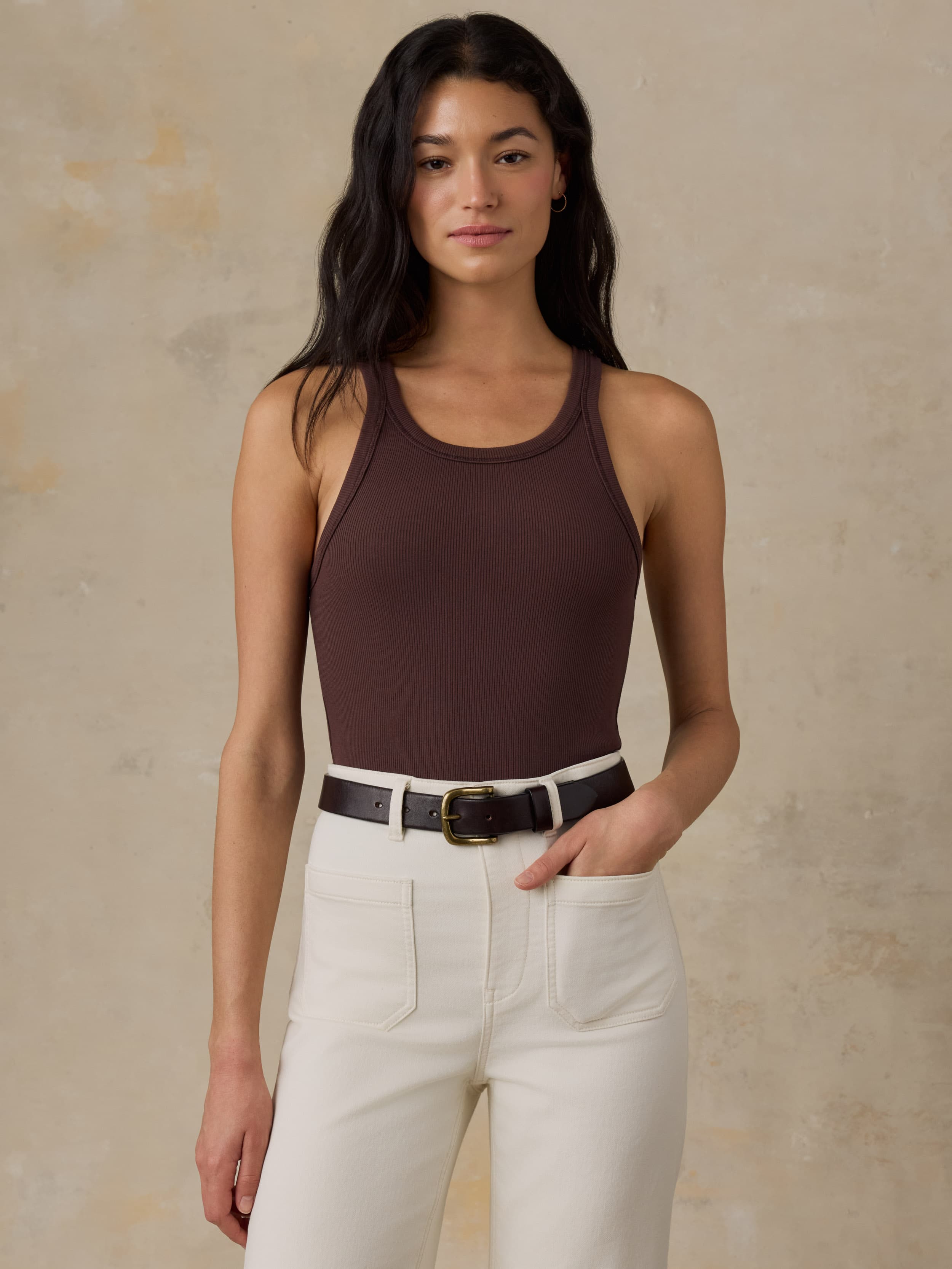 Woman wearing a brown tank top and white jeans against a beige background