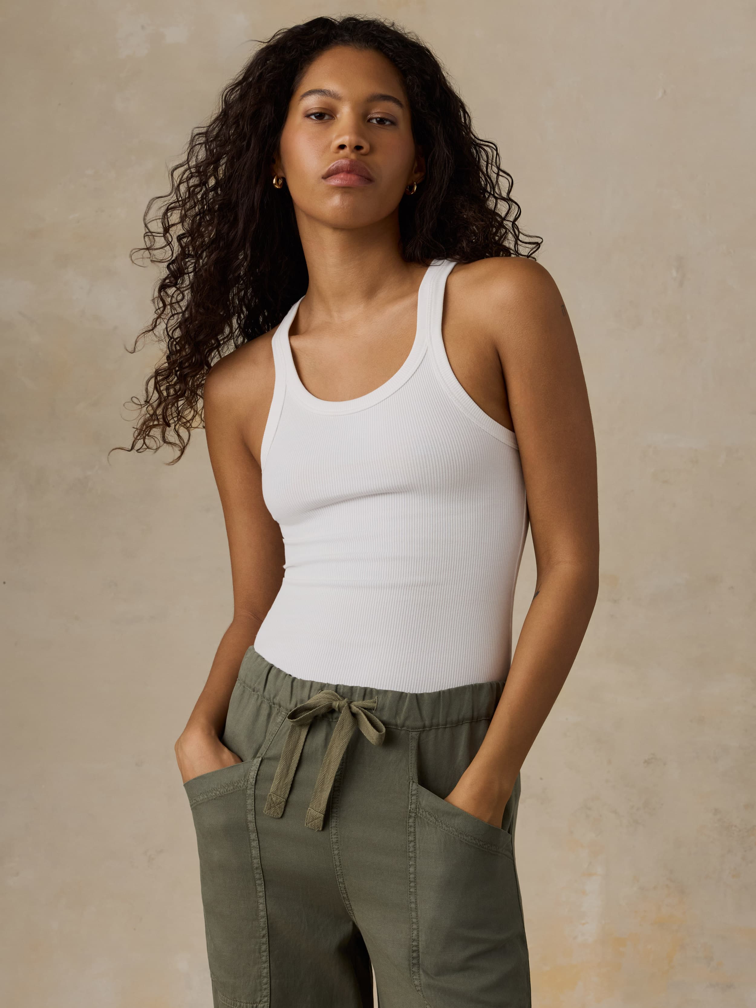 Woman wearing a white tank top and green pants against a beige background