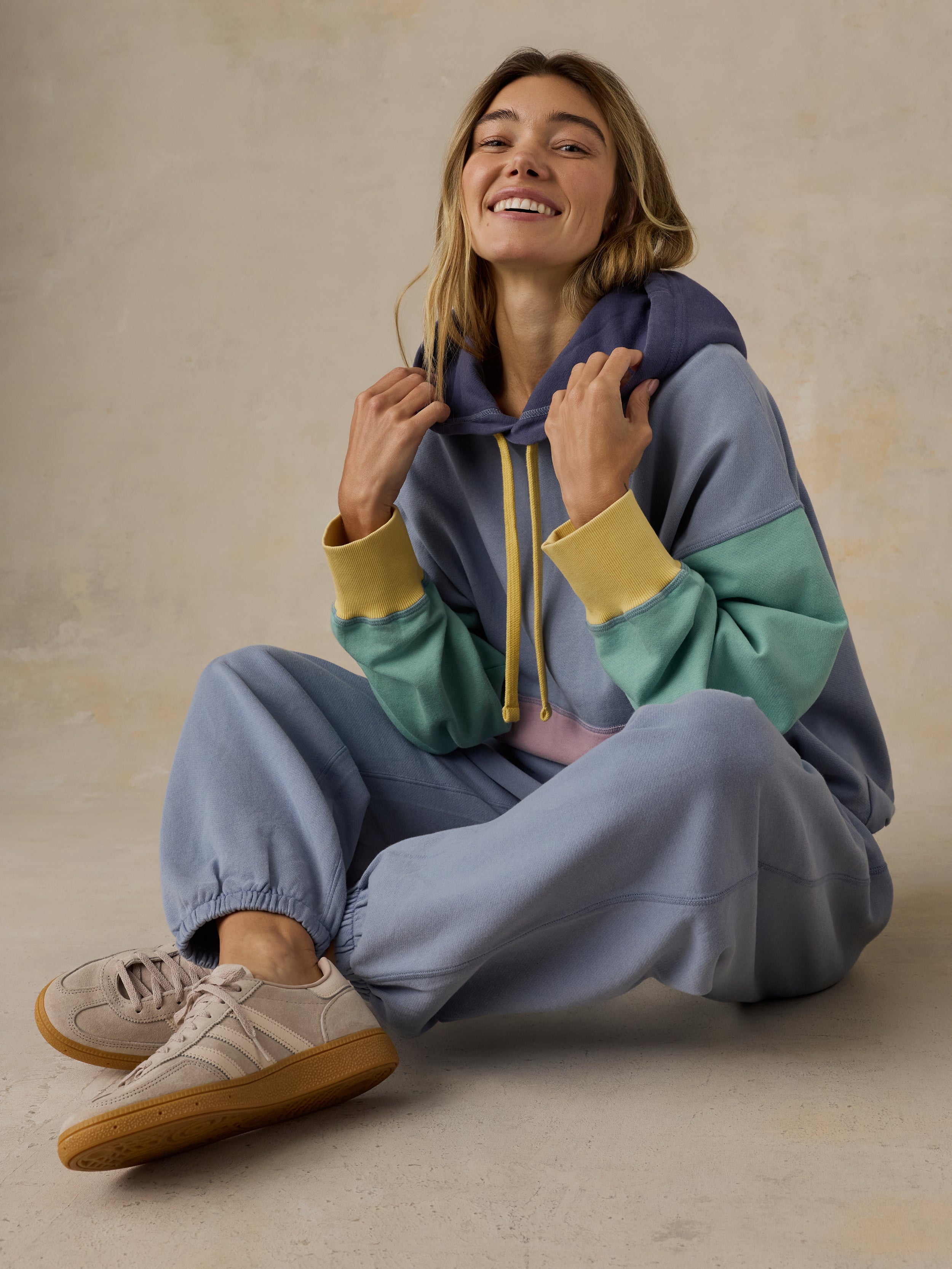 Woman wearing a colorful hoodie and sweatpants sitting on the floor.